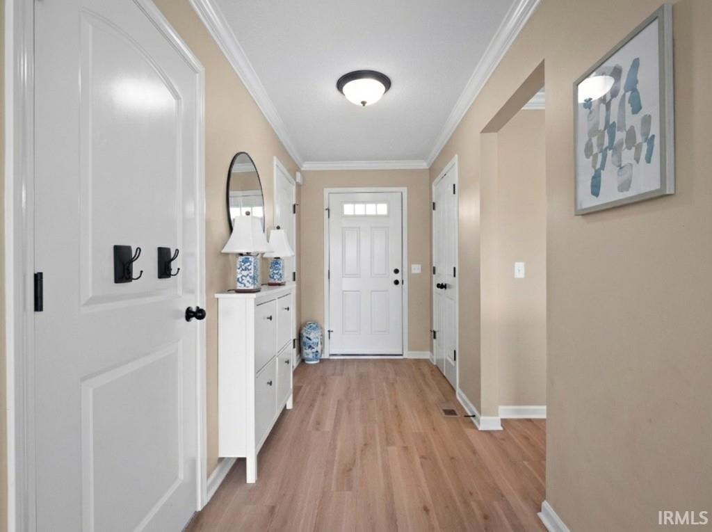Doorway to outside with crown molding and wood finished floors
