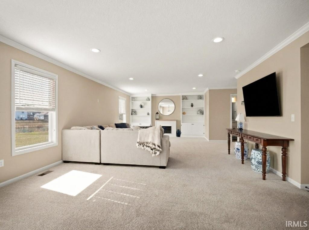 Carpeted living room featuring a fireplace, ornamental molding, recessed lighting, and built in shelves