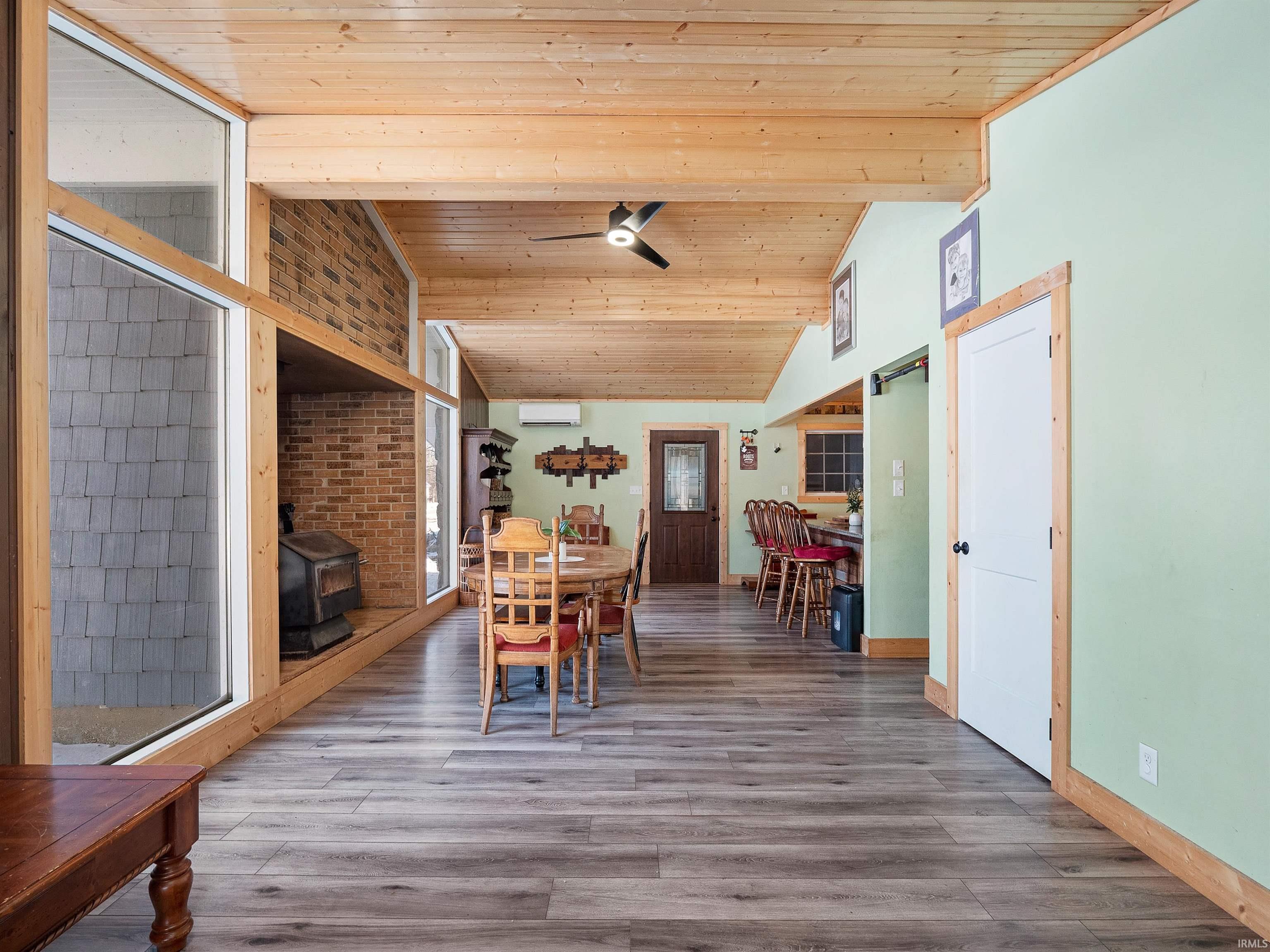 Dining room featuring a wood stove, vaulted ceiling, wood ceiling, wood finished floors, and ceiling fan