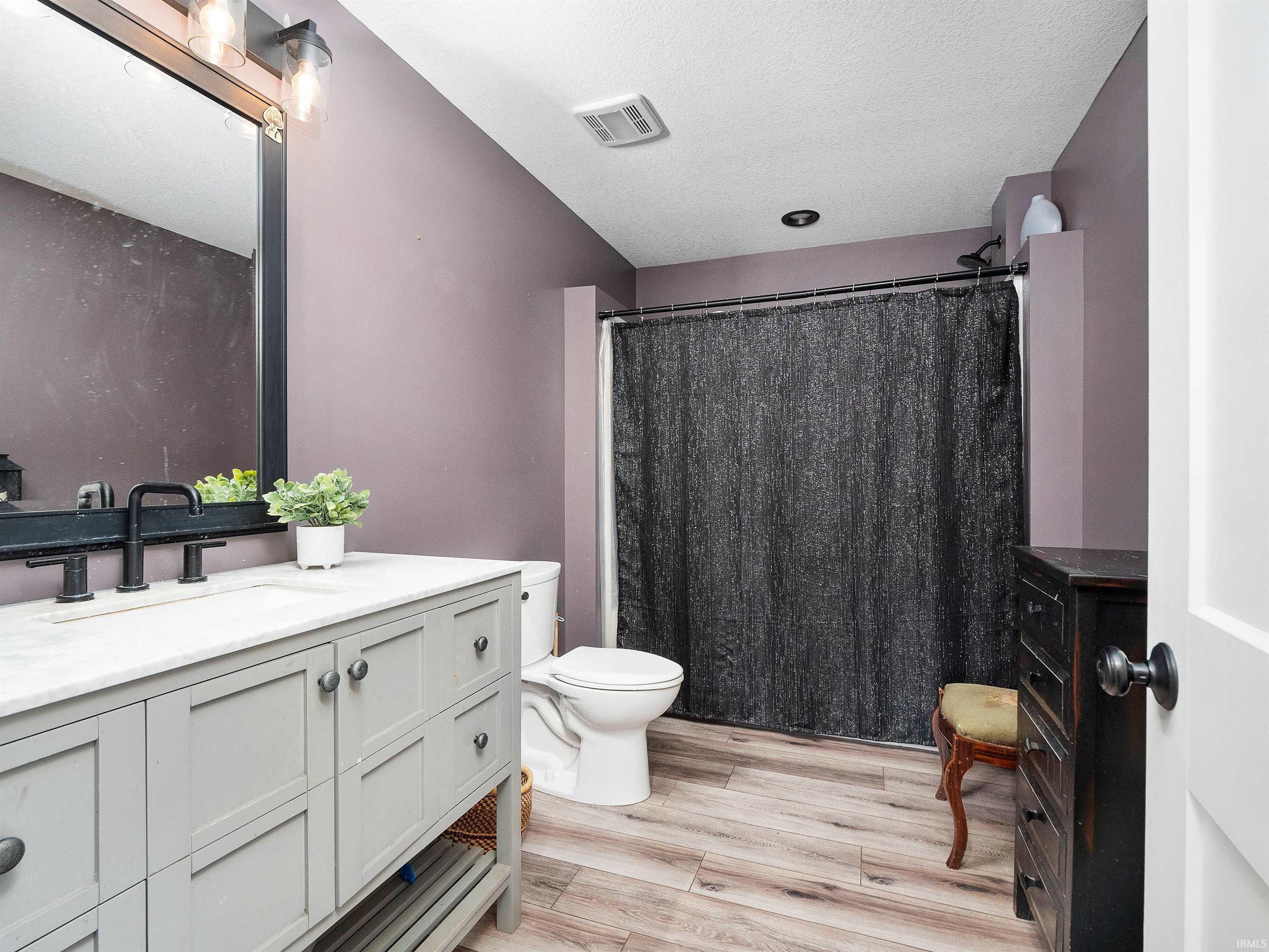 Full bathroom featuring vanity, a shower with curtain, light wood finished floors, and a textured ceiling