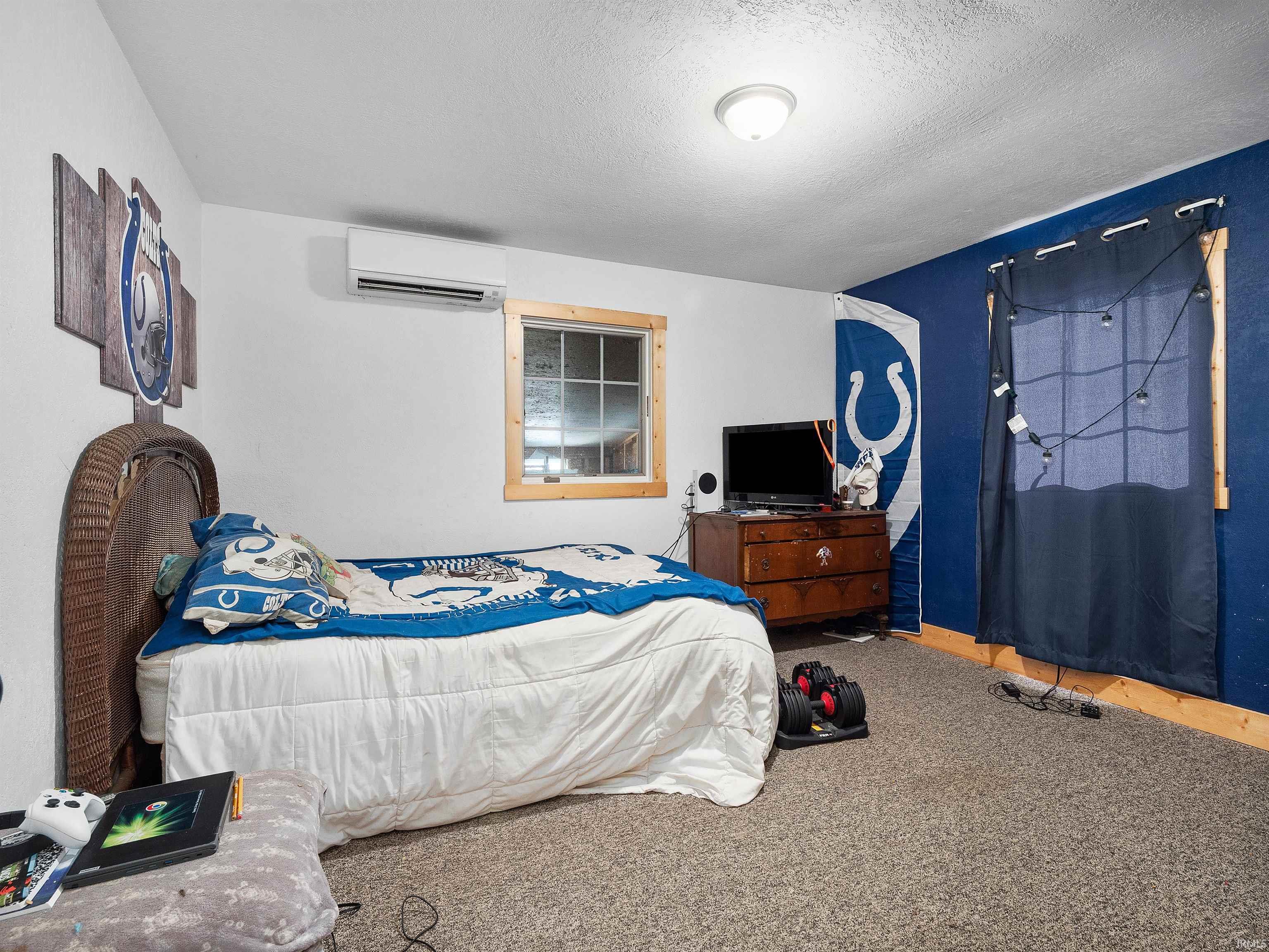 Carpeted bedroom featuring a textured ceiling and a wall mounted AC