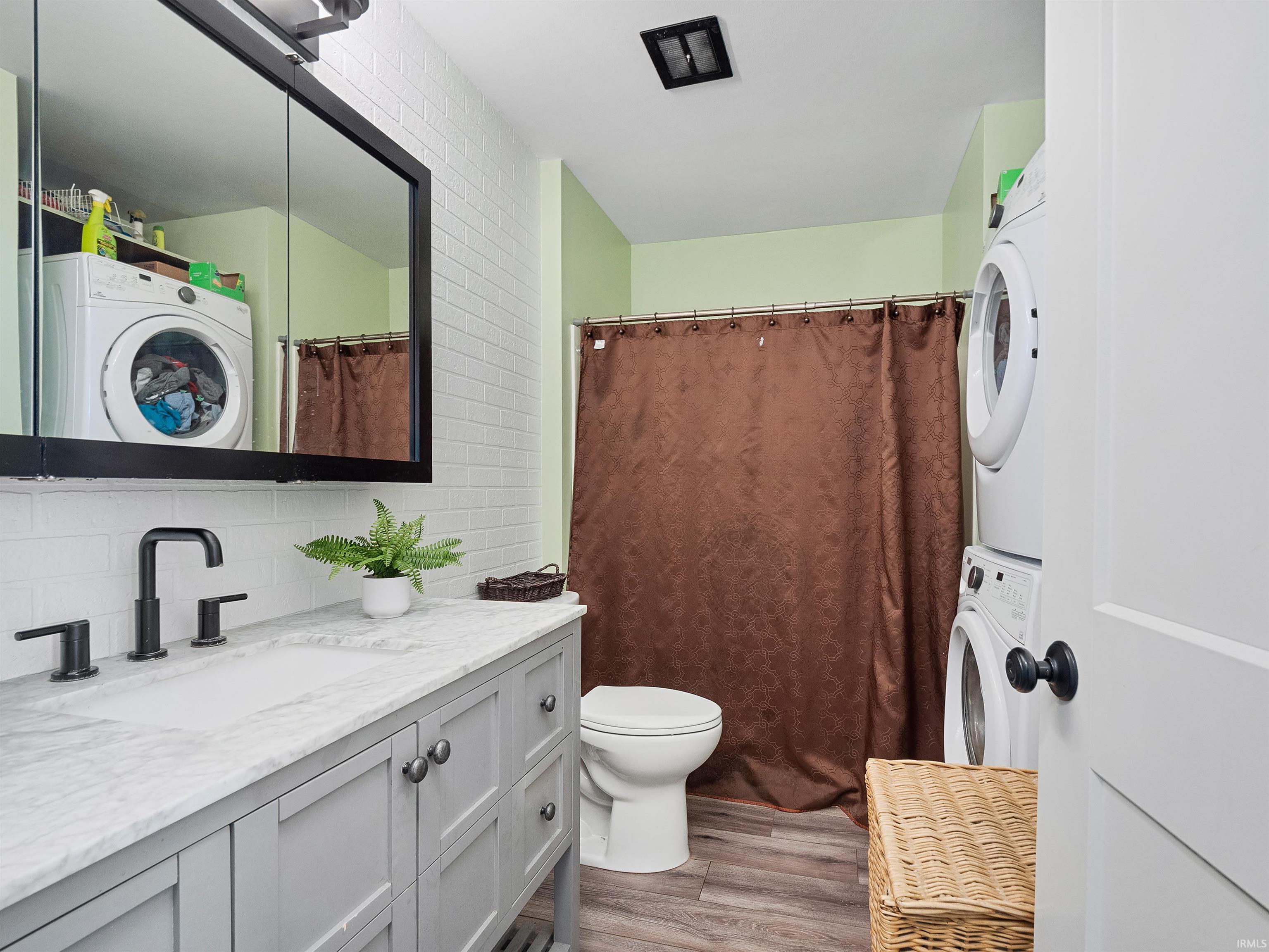 Full bath featuring stacked washer and clothes dryer, light wood-type flooring, vanity, a shower with shower curtain, and tasteful backsplash