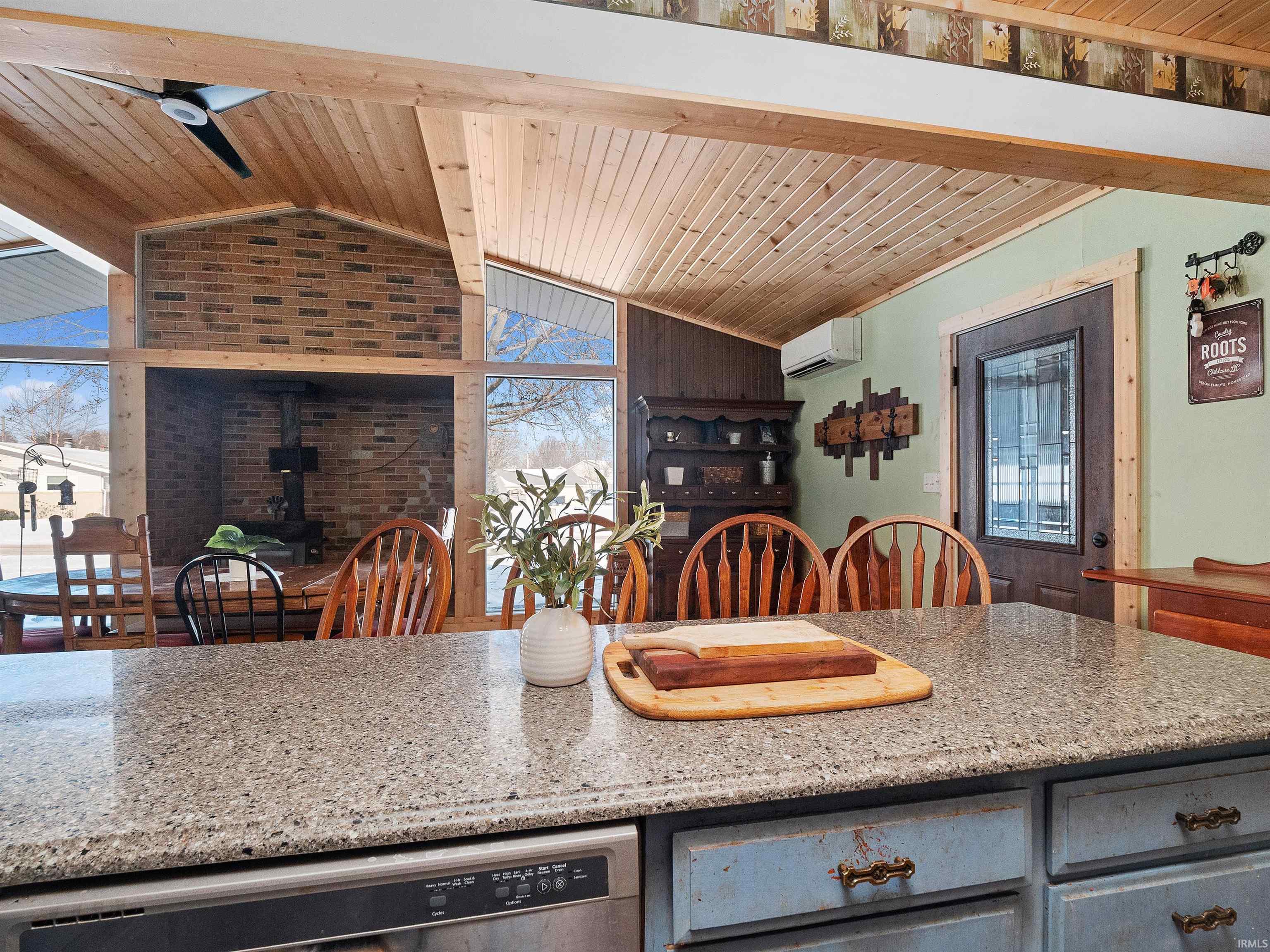 Kitchen with a wood stove, wood ceiling, light stone countertops, stainless steel dishwasher, and ceiling fan