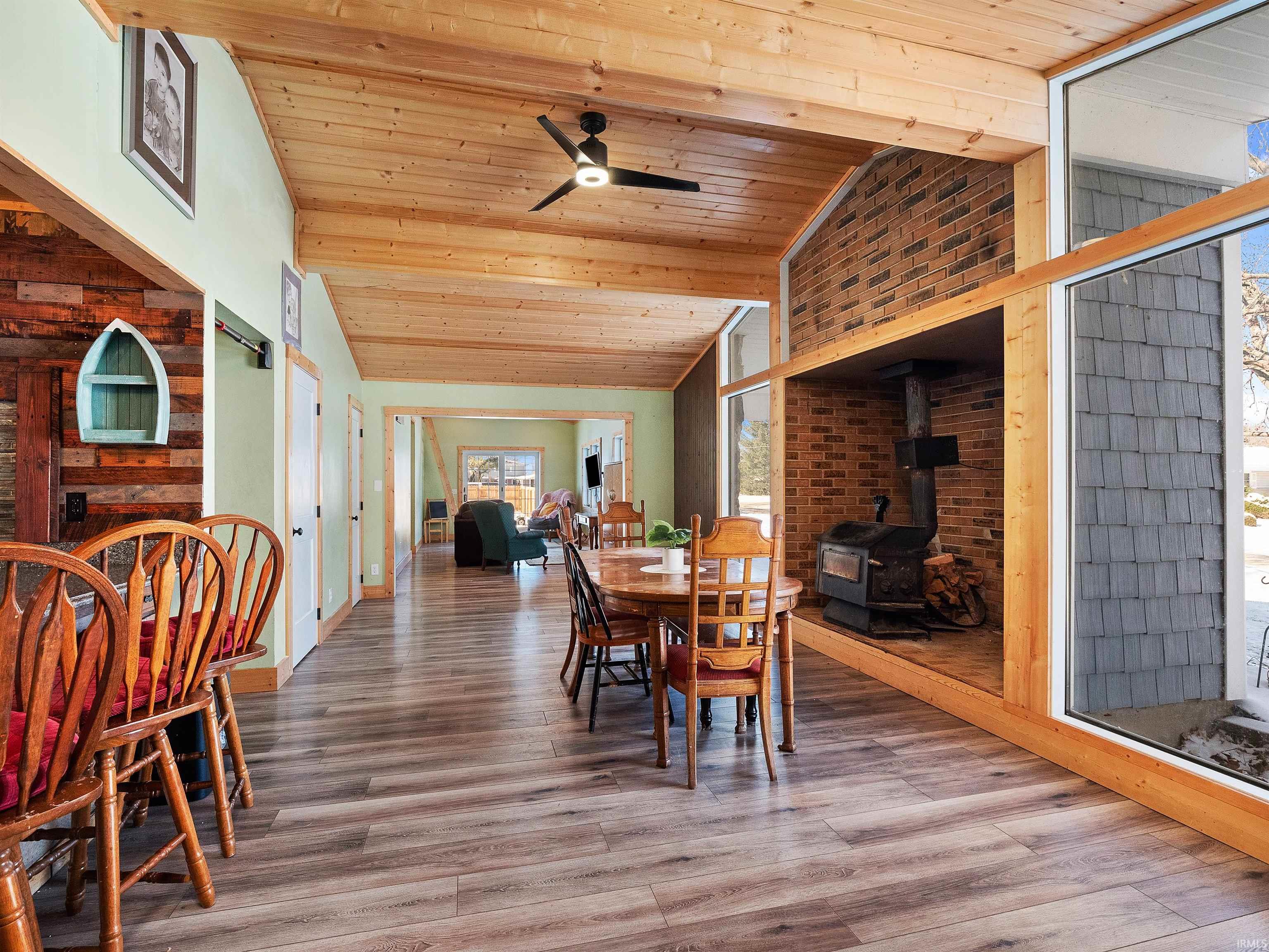Dining area featuring a wood stove, light wood-style flooring, wood ceiling, a ceiling fan, and high vaulted ceiling