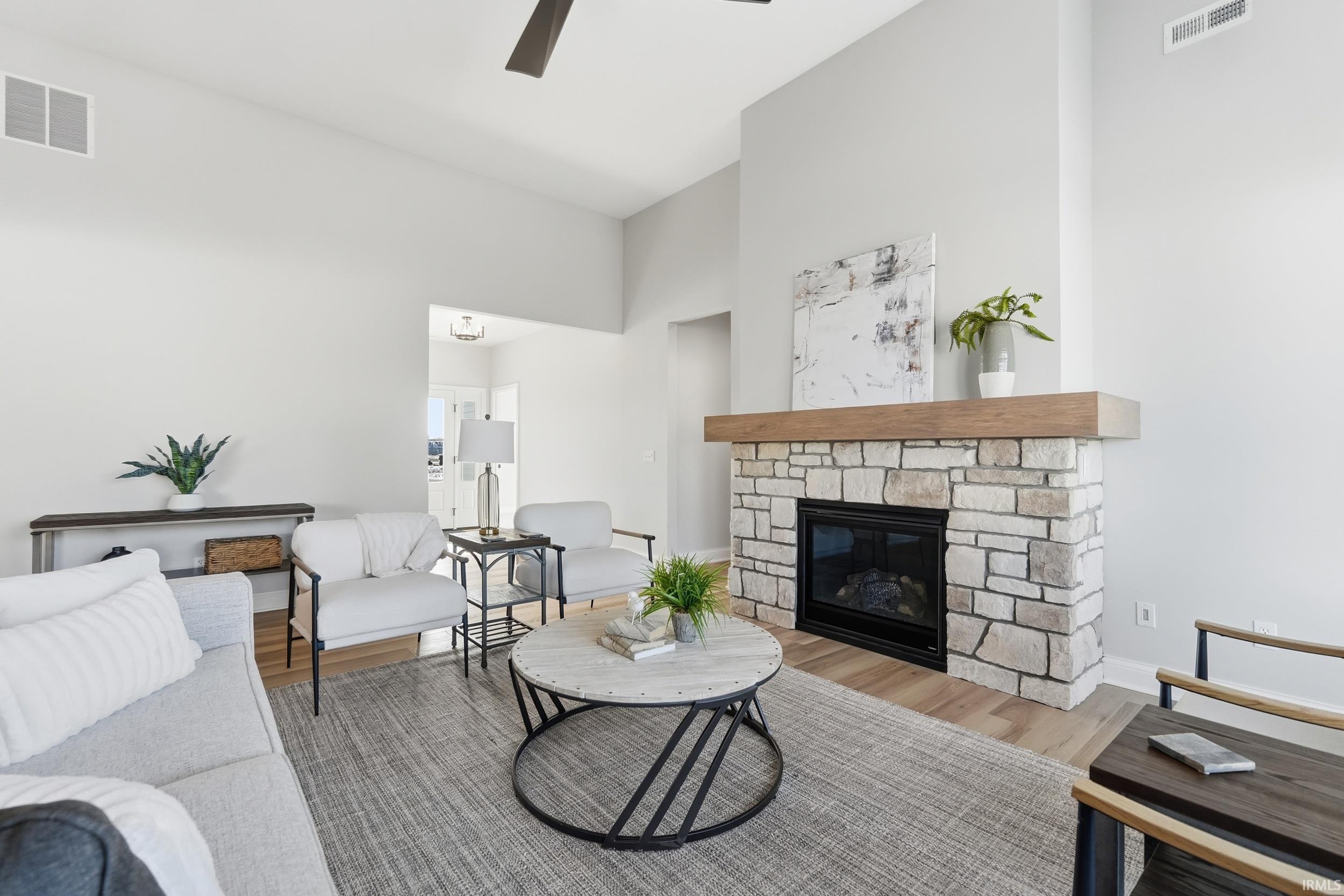 Living room with wood finished floors, a high ceiling, a stone fireplace, and ceiling fan
