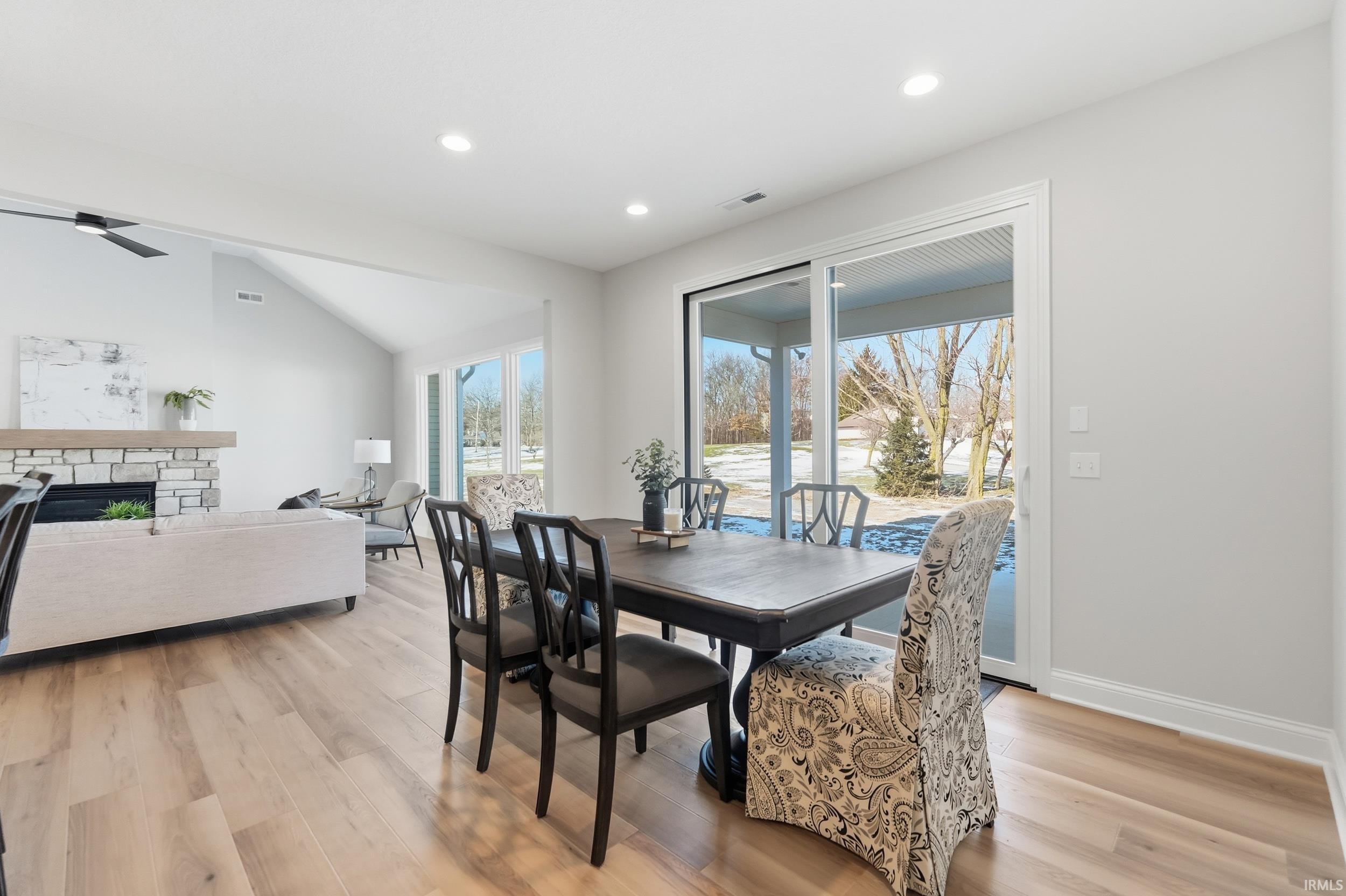 Dining space with light wood-style flooring, a stone fireplace, recessed lighting, and lofted ceiling