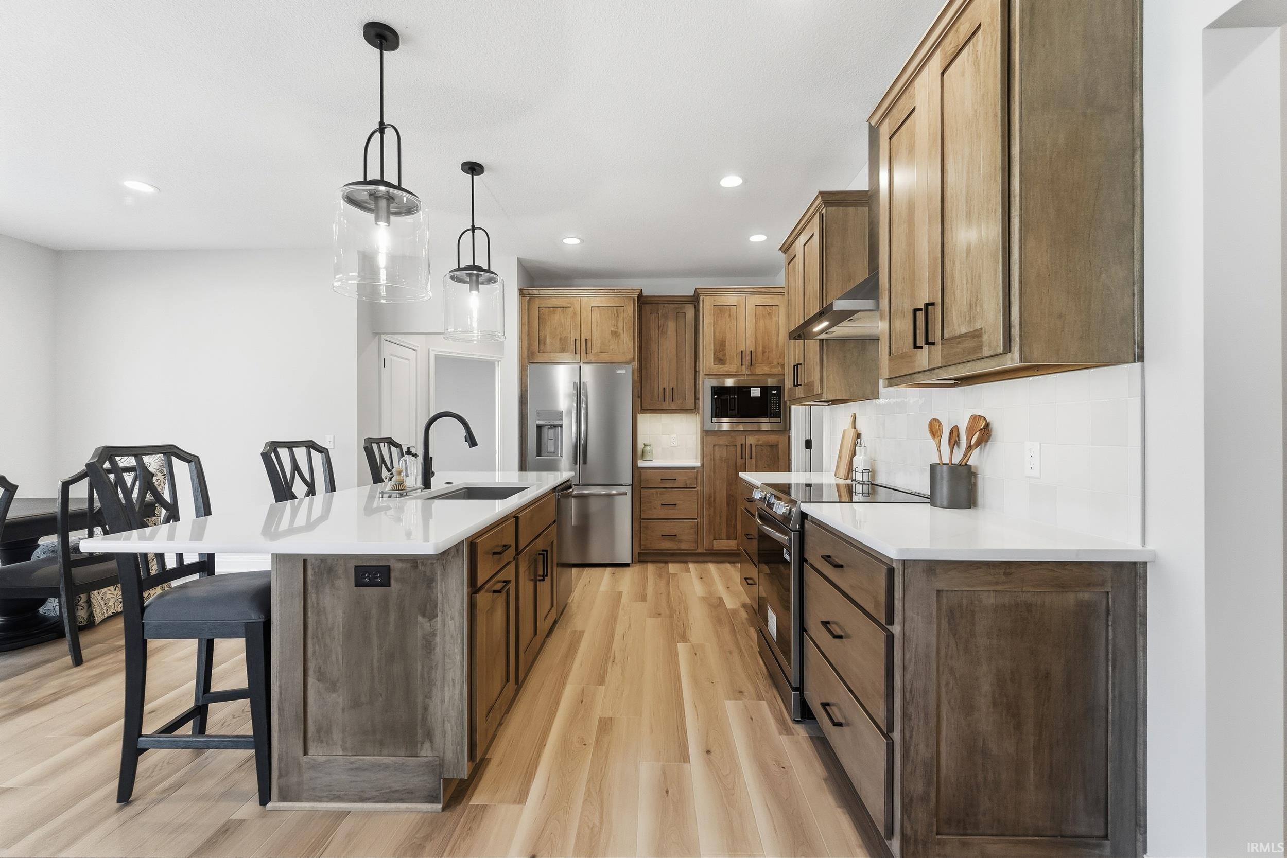 Kitchen with a kitchen bar, stainless steel appliances, an island with sink, pendant lighting, and decorative backsplash
