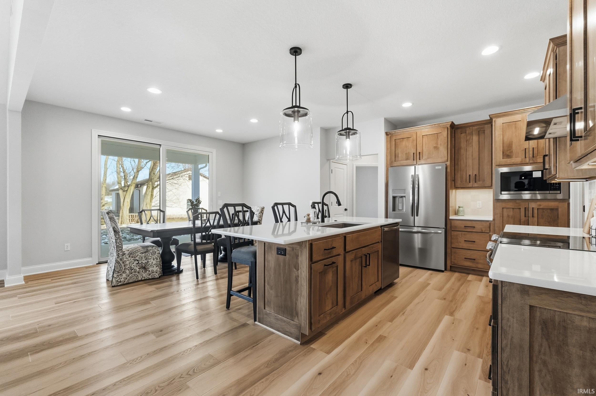 Kitchen with a kitchen breakfast bar, appliances with stainless steel finishes, hanging light fixtures, a center island with sink, and light stone countertops