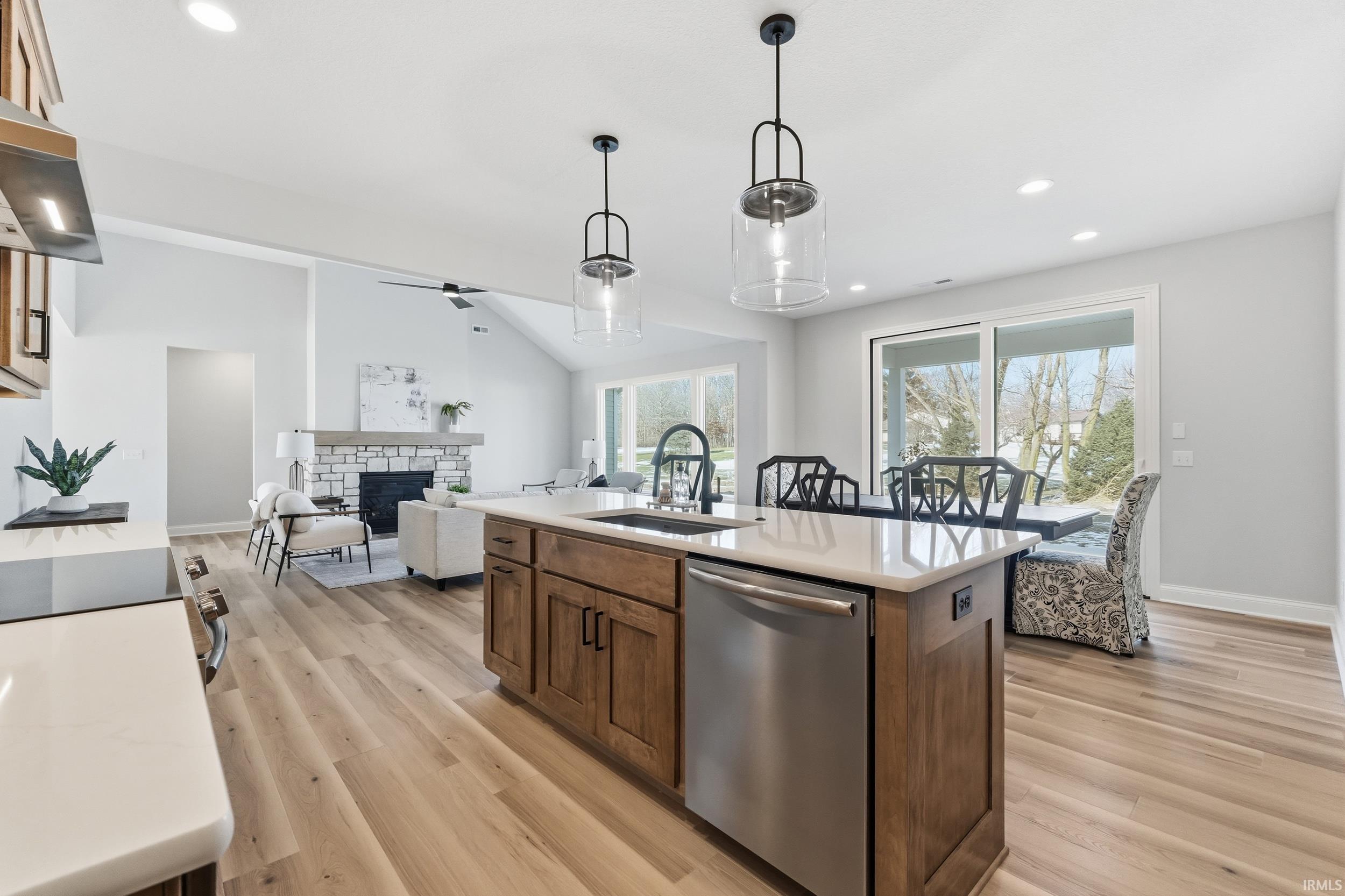 Kitchen with stainless steel dishwasher, a stone fireplace, open floor plan, recessed lighting, and hanging light fixtures