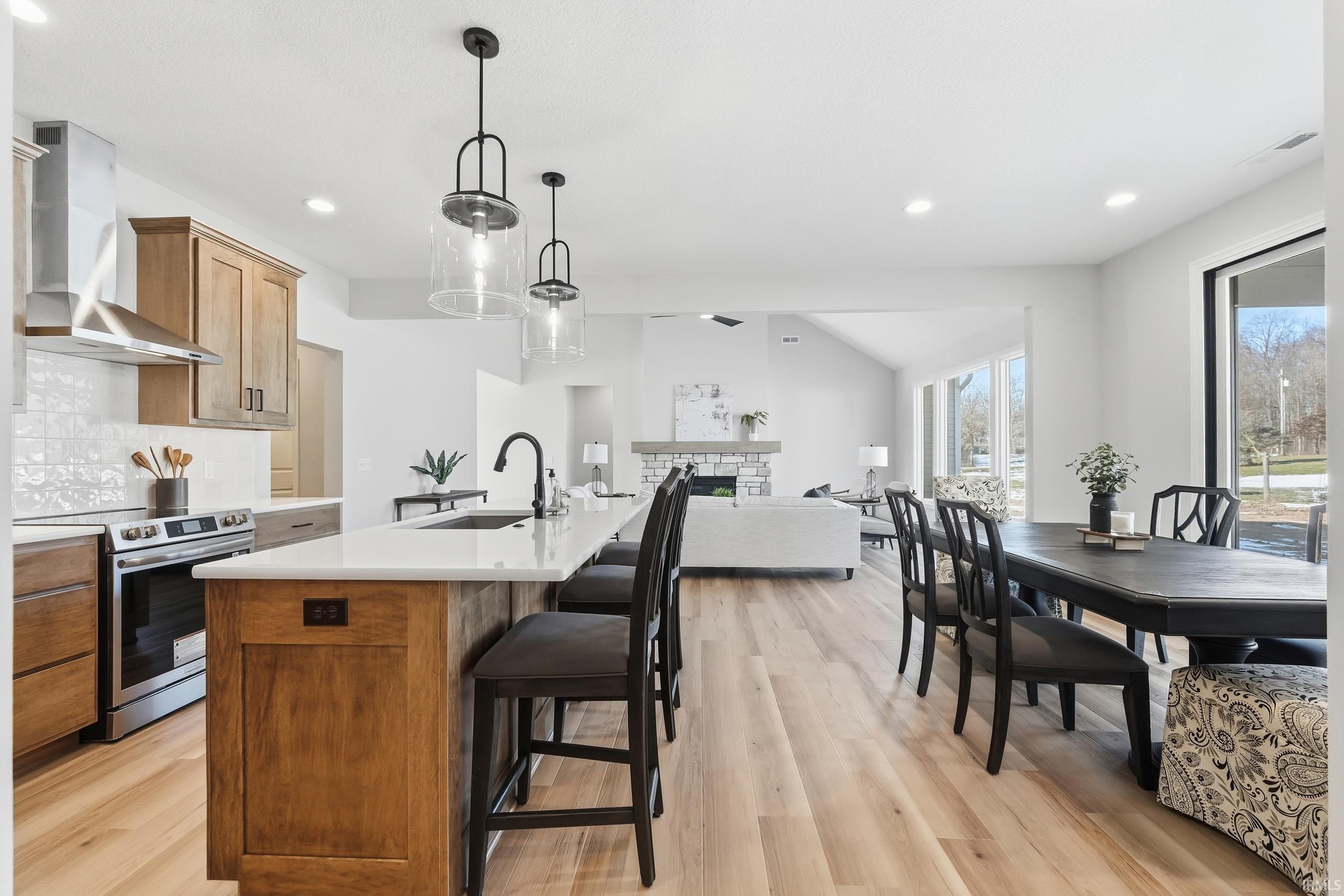 Kitchen with stainless steel range with electric cooktop, a center island with sink, pendant lighting, wall chimney exhaust hood, and a kitchen breakfast bar