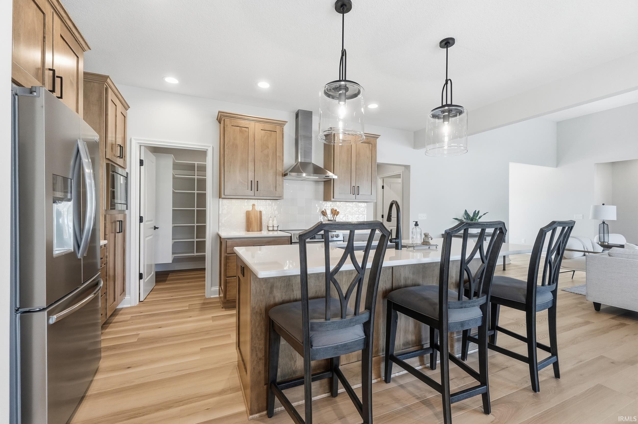 Kitchen featuring appliances with stainless steel finishes, an island with sink, decorative light fixtures, a breakfast bar area, and wall chimney exhaust hood