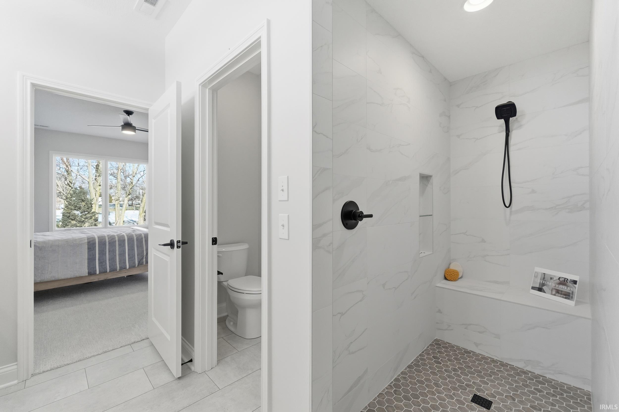 Bathroom featuring a marble finish shower, connected bathroom, light tile patterned flooring, ceiling fan, and light colored carpet