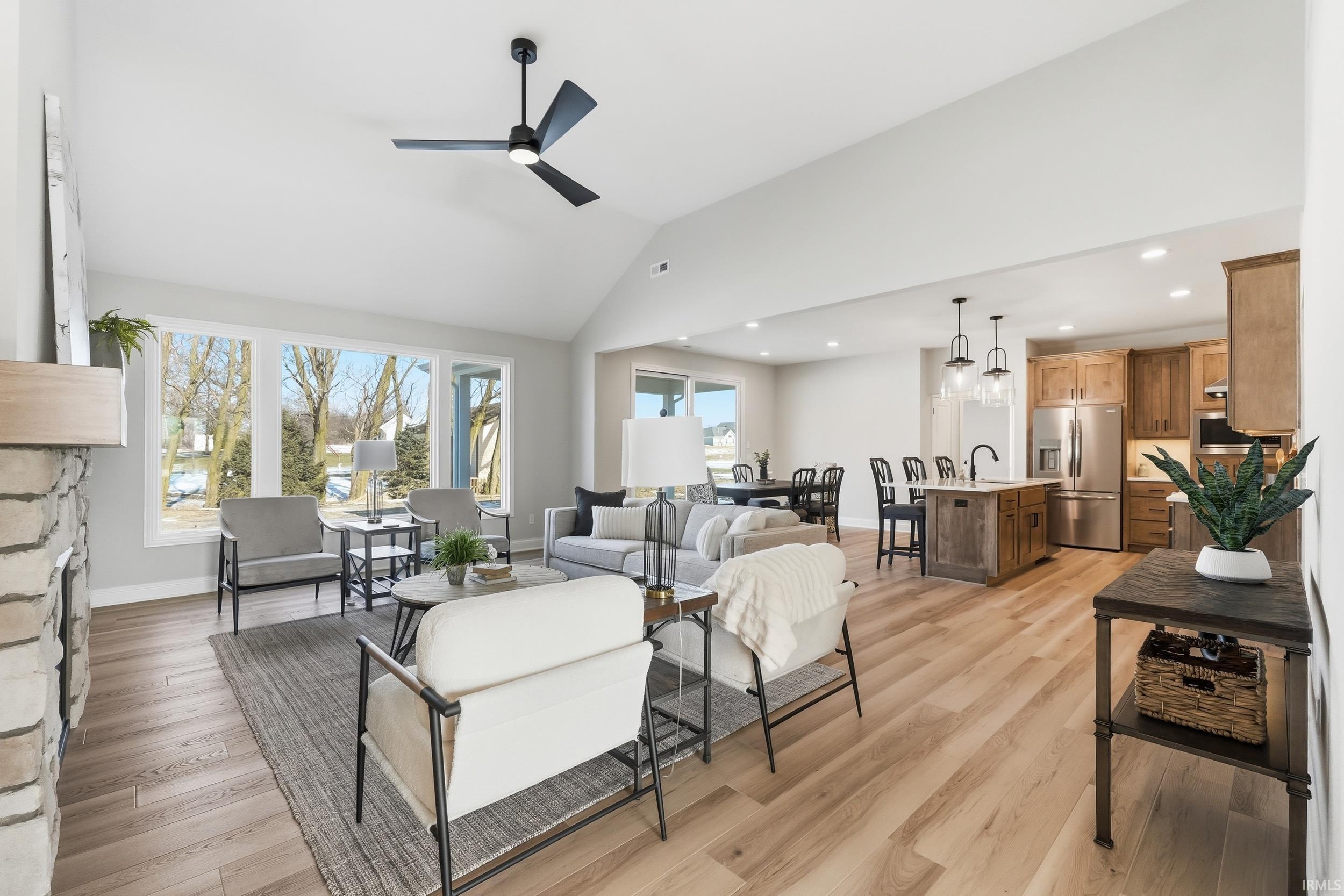 Living room with light wood-style flooring, high vaulted ceiling, ceiling fan, a stone fireplace, and recessed lighting