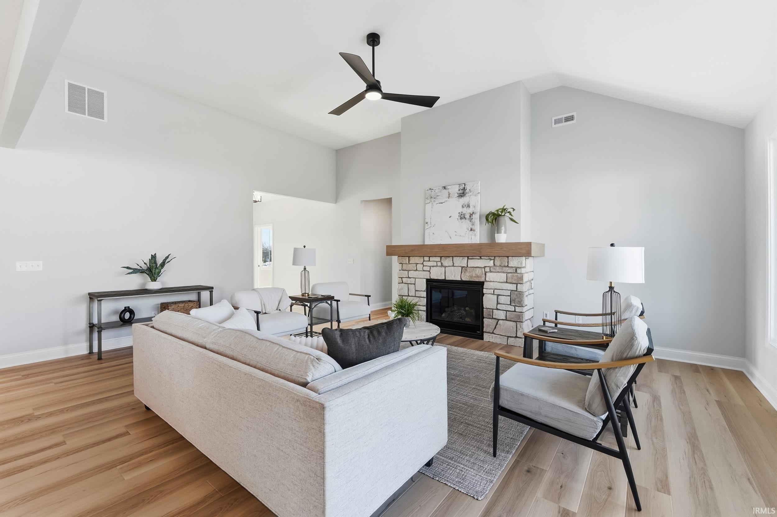 Living room featuring a fireplace, light wood finished floors, high vaulted ceiling, and ceiling fan
