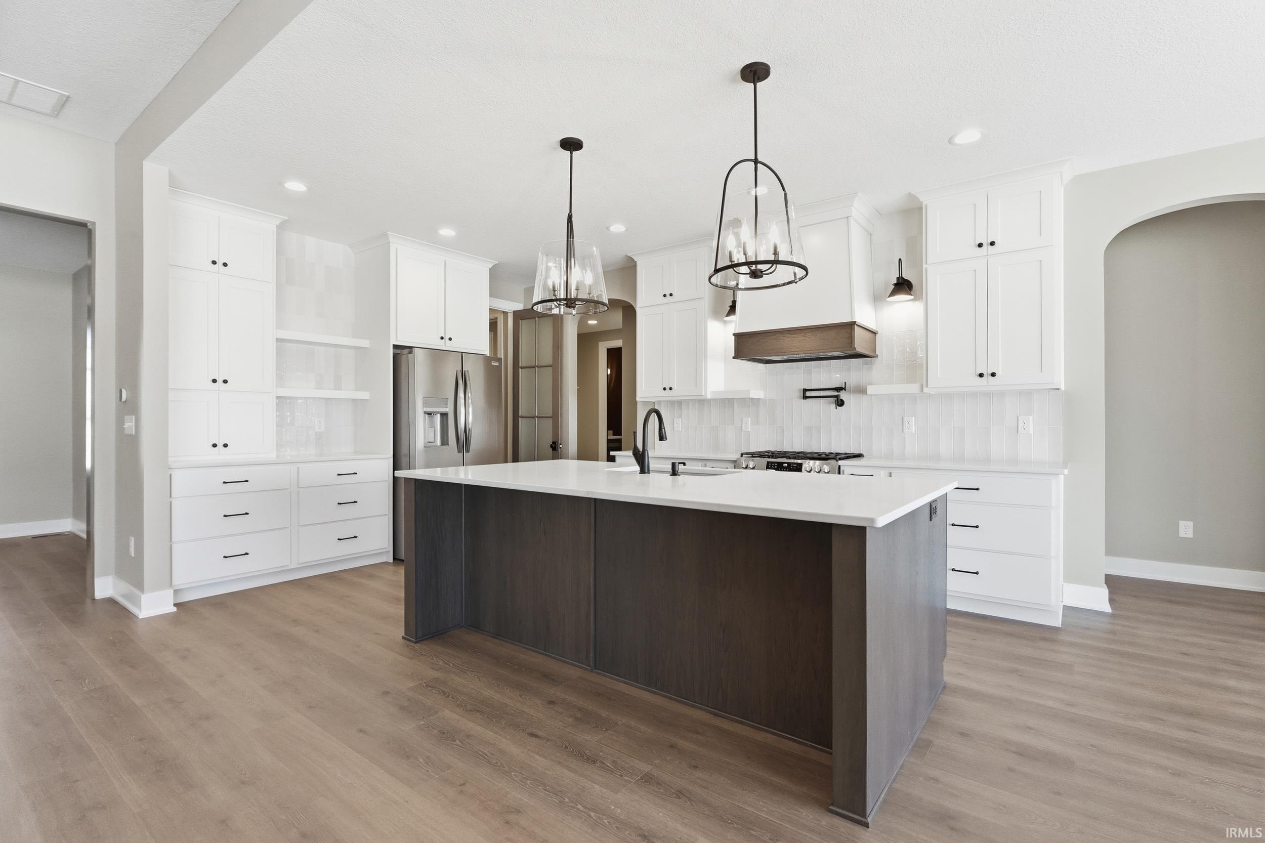 Kitchen with arched walkways, open floor plan, a chandelier, quartz countertops, and a center island with sink
