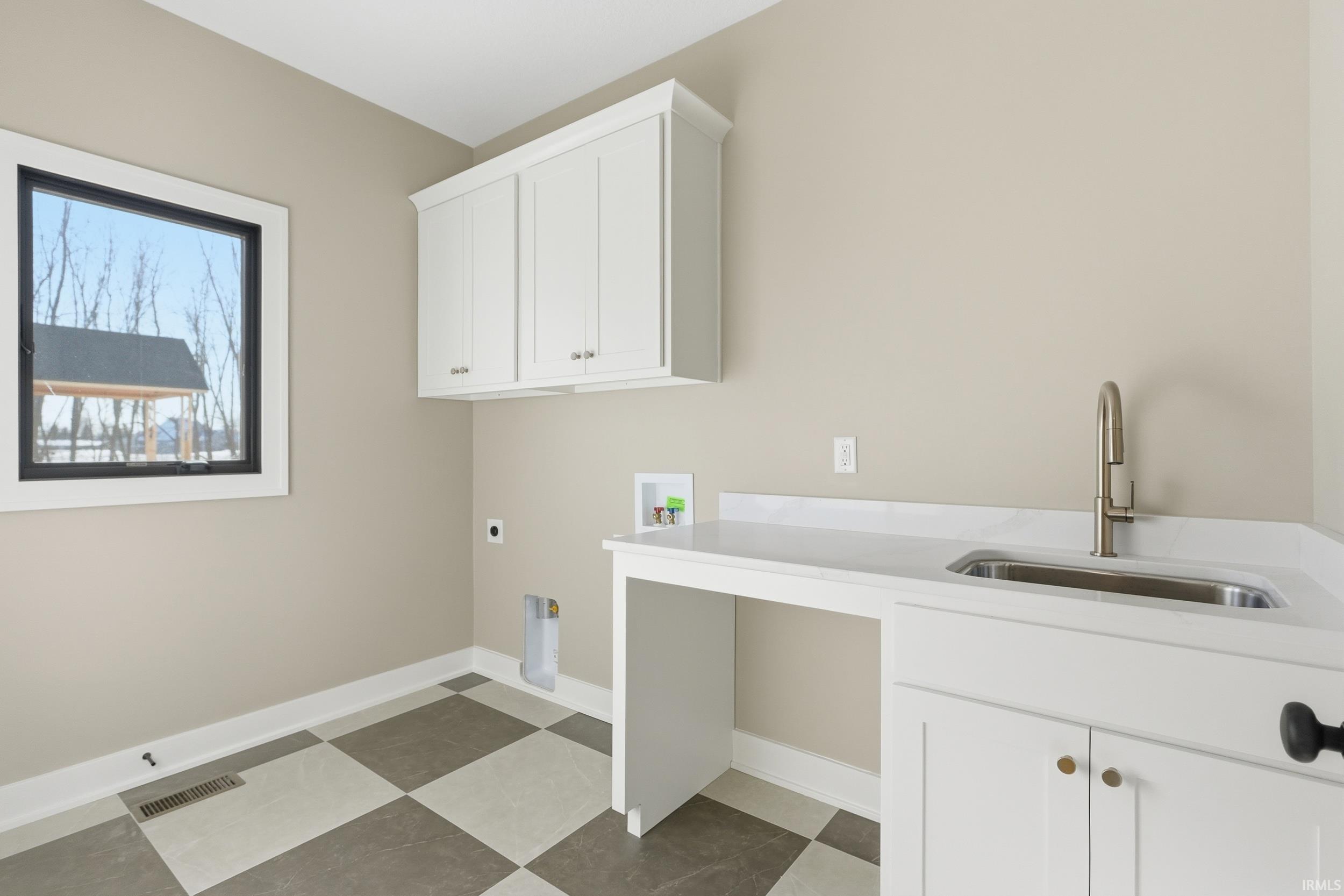 Laundry area with checkered flooring, sink, cabinets and a closet for storage
