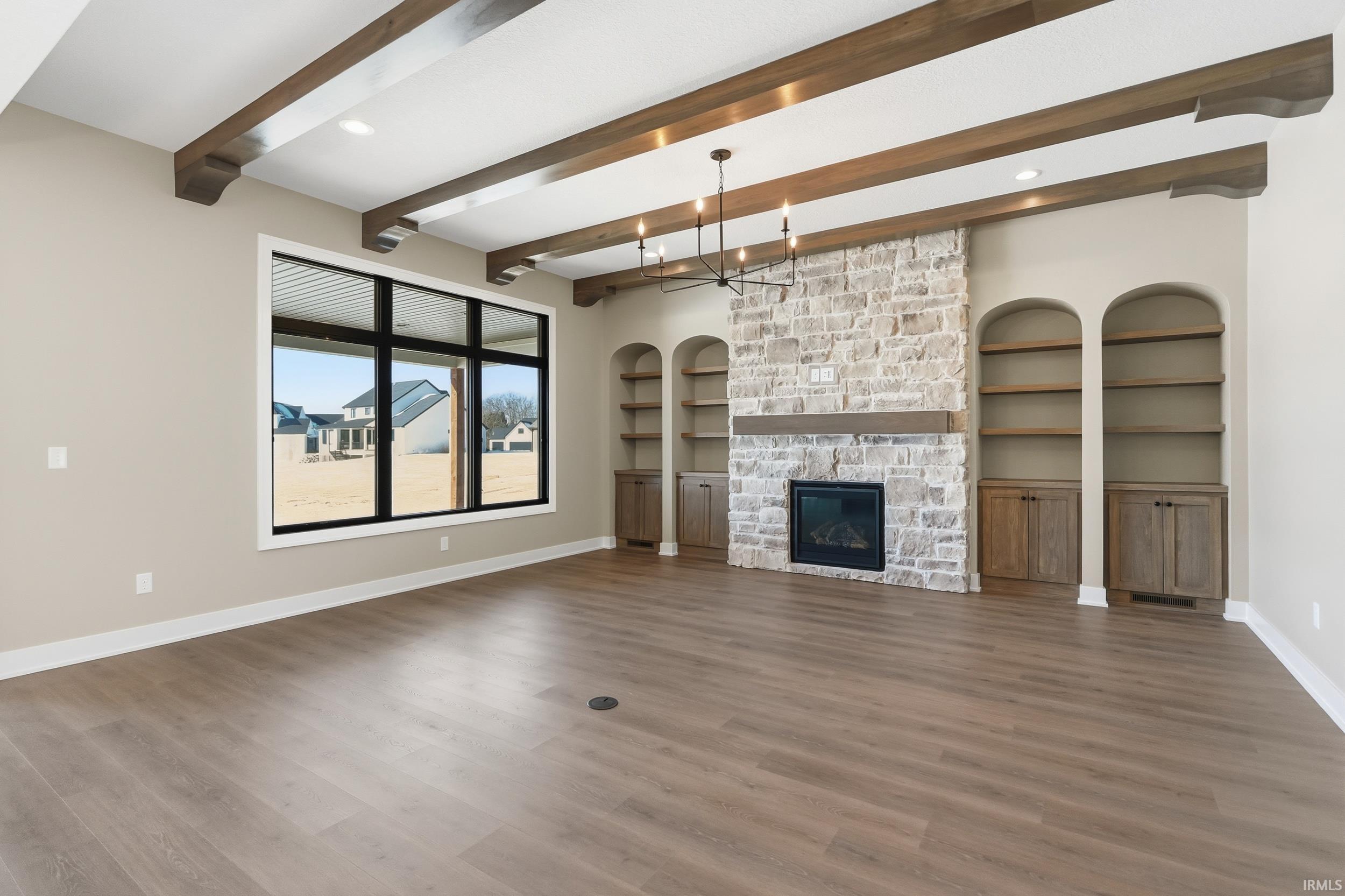 Living room with arched built in features, a stone fireplace, light wood finished floors, a chandelier, and beamed ceiling