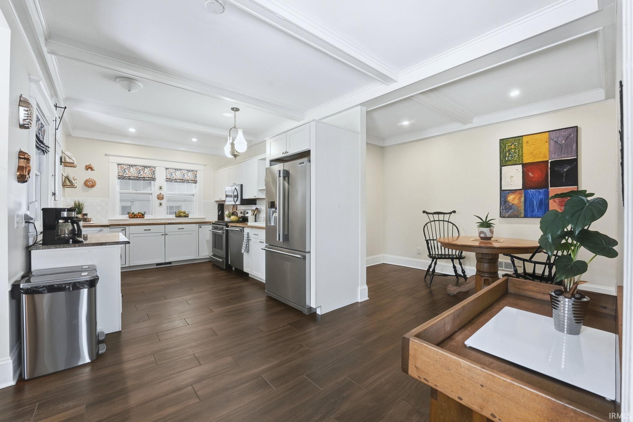 Kitchen featuring white cabinets, dark wood-style flooring, beamed ceiling, appliances with stainless steel finishes, and pendant lighting