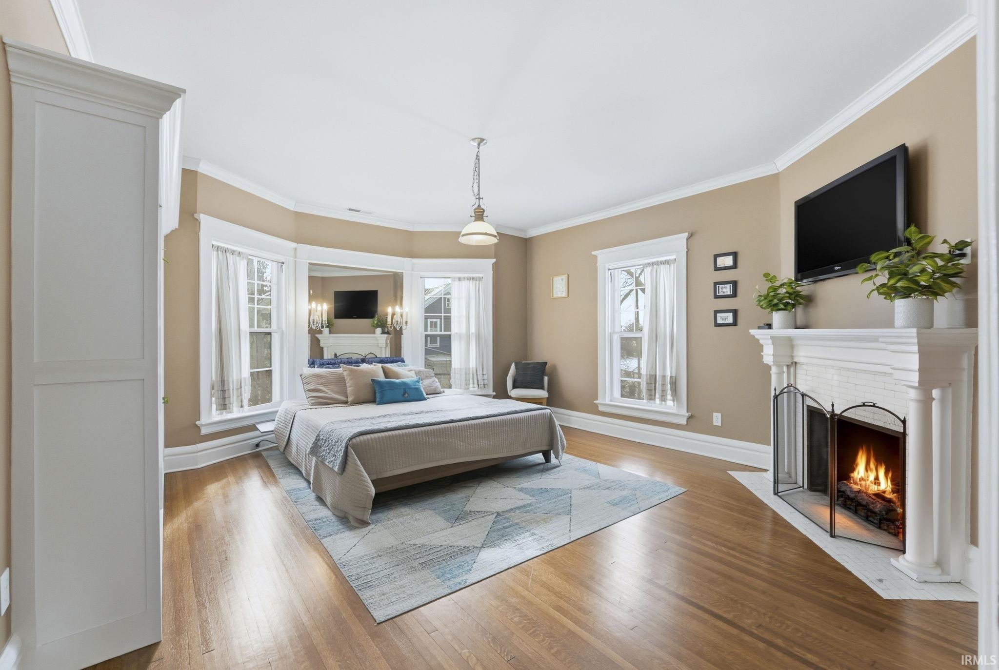 Bedroom with hardwood / wood-style floors, multiple windows, a fireplace with flush hearth, and crown molding