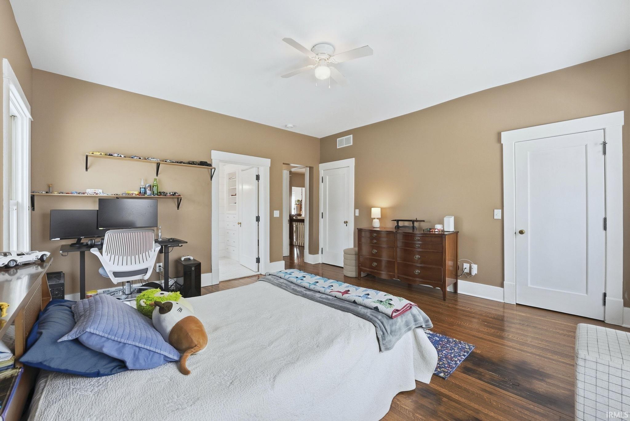 Bedroom with dark wood-type flooring, ceiling fan, ensuite bathroom, and a desk