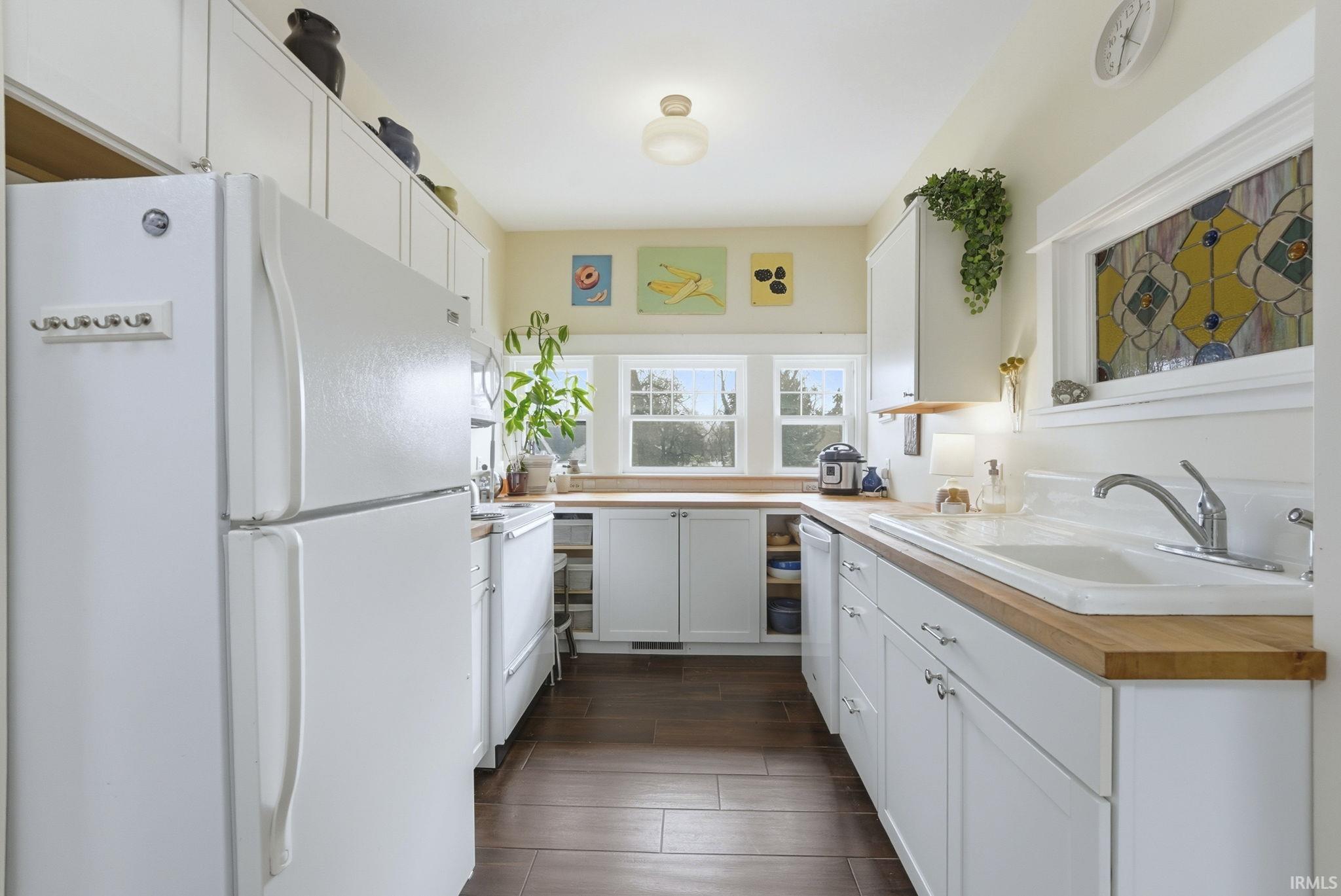 Kitchen with white appliances, white cabinetry, dark wood finished floors, and wood counters
