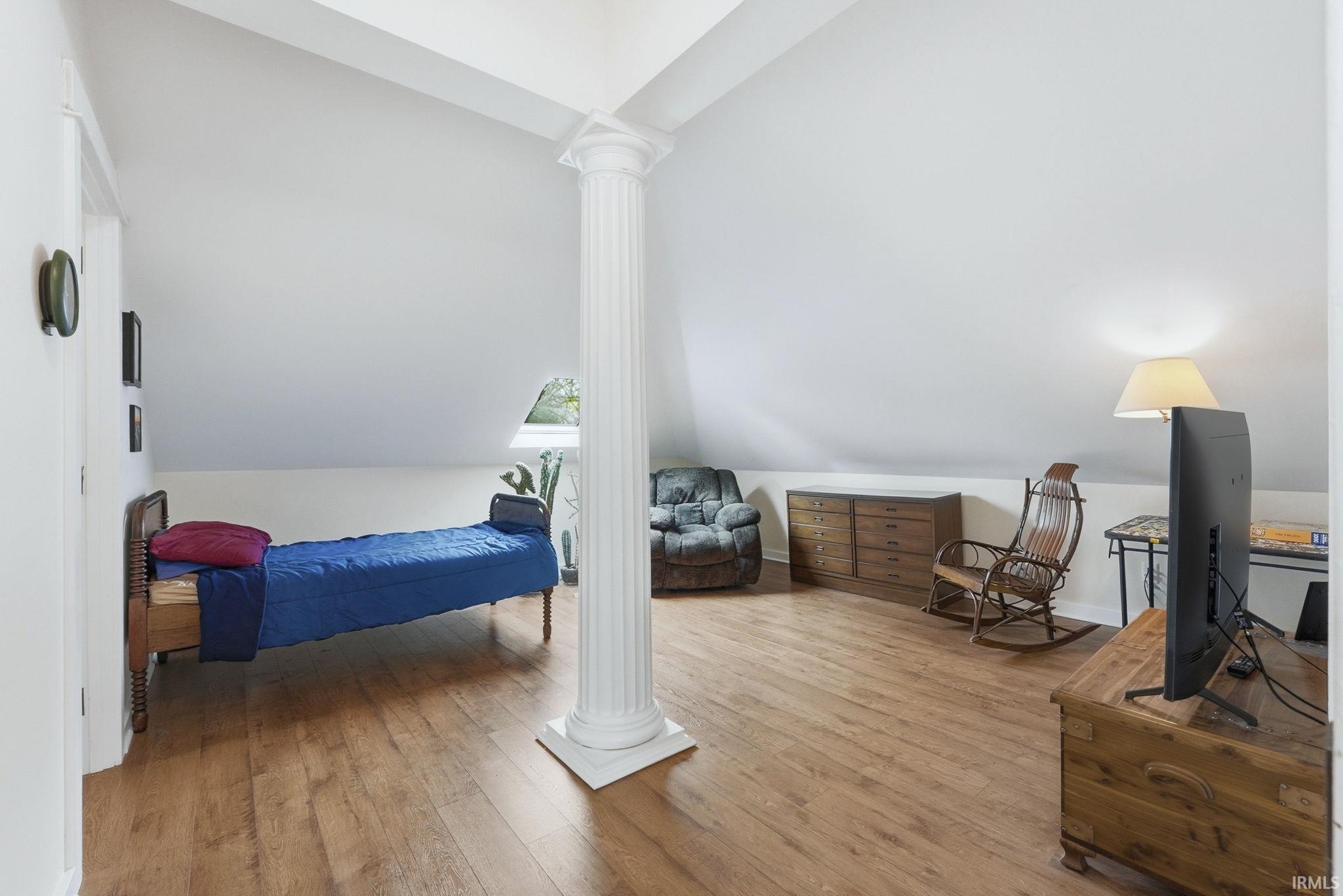 Bedroom featuring light wood-style flooring, vaulted ceiling, and ornate columns