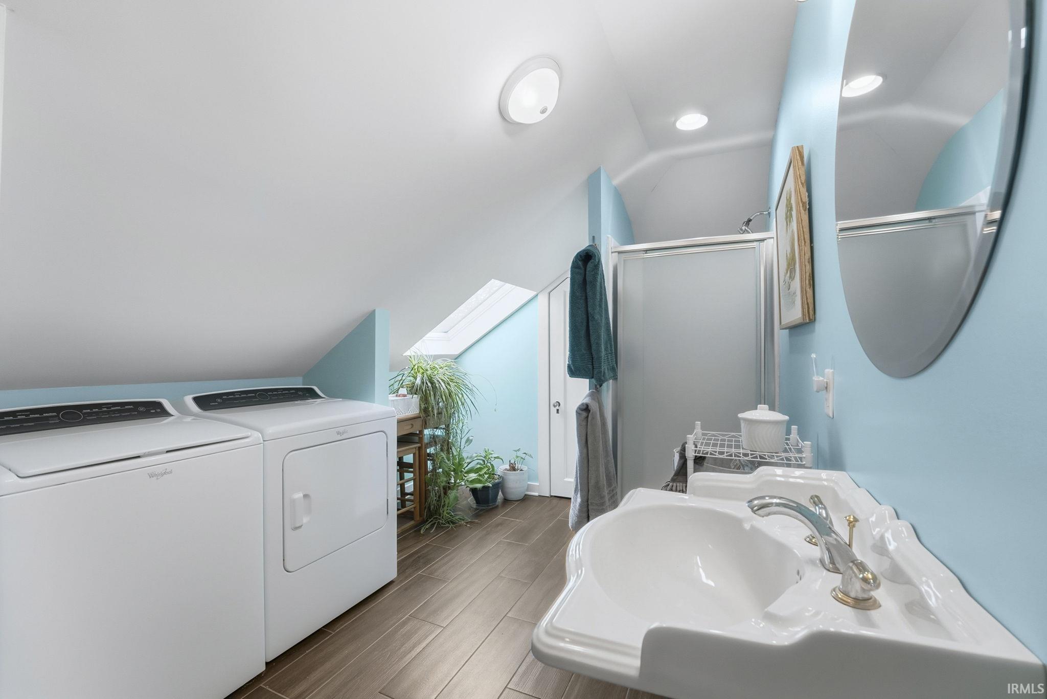 Bathroom featuring lofted ceiling, washer and dryer, a stall shower, wood tiled floors, and a skylight