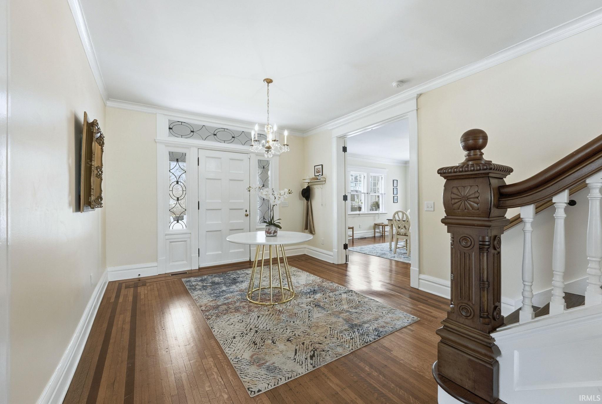 Foyer with dark wood-style flooring, crown molding, a chandelier, and stairway