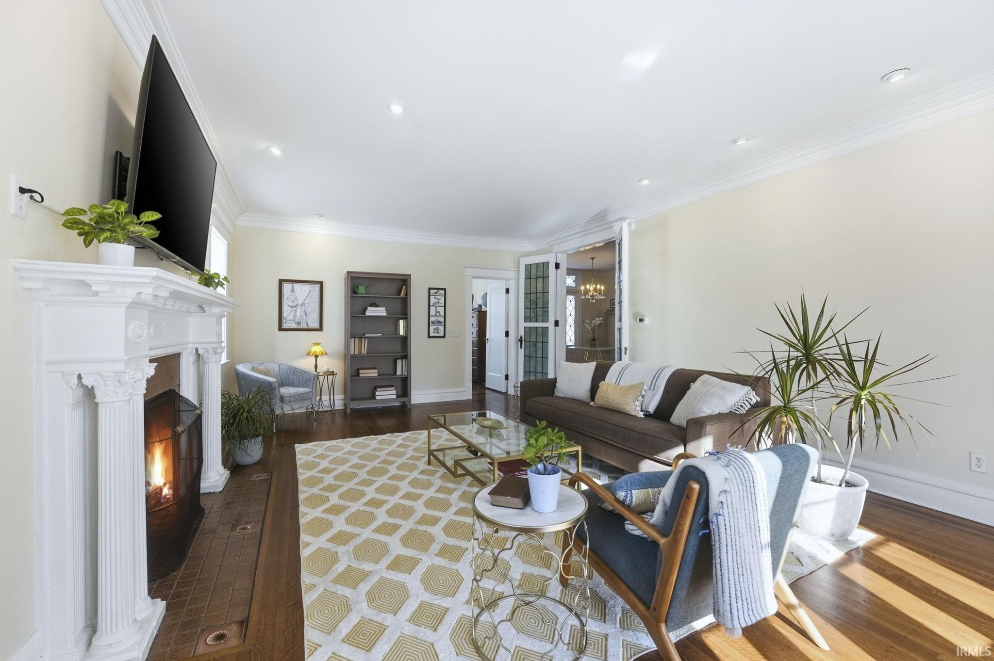 Living area with a lit fireplace, crown molding, dark wood-type flooring, and a chandelier
