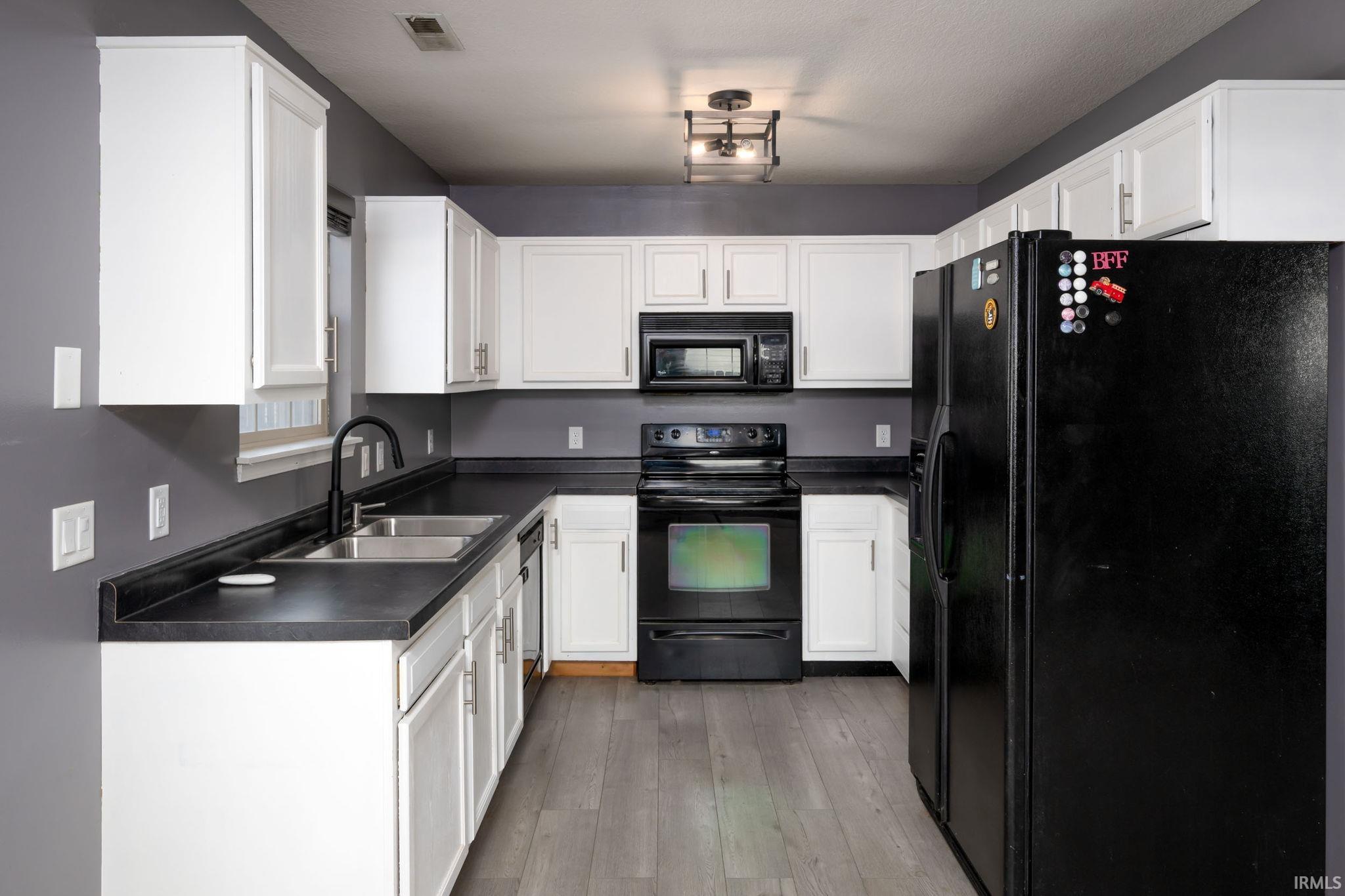 Kitchen featuring black appliances, white cabinets, light wood-style floors, and dark countertops