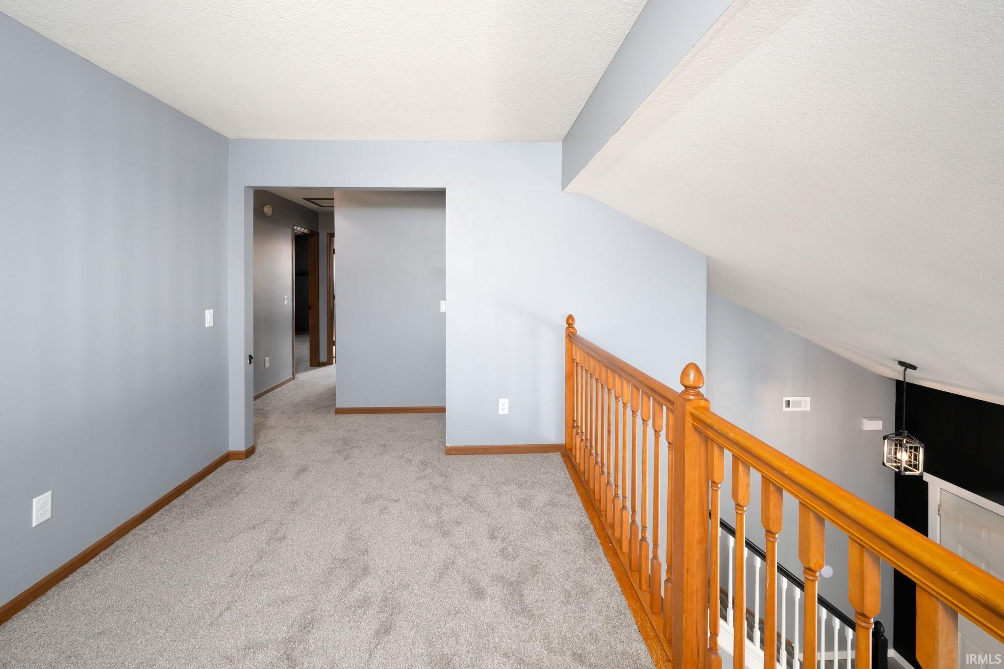 Corridor with an upstairs landing, light carpet, and a textured ceiling