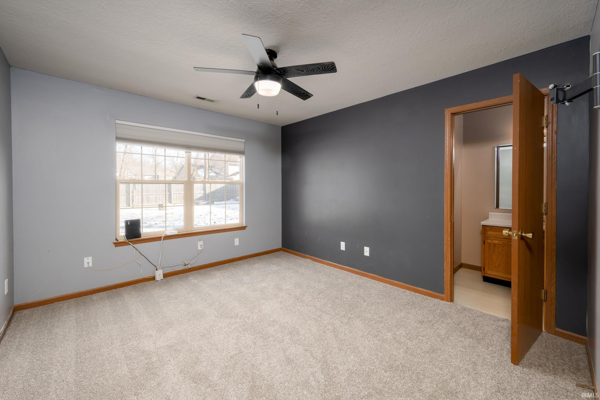 Unfurnished bedroom featuring light carpet, ceiling fan, a textured ceiling, and ensuite bathroom