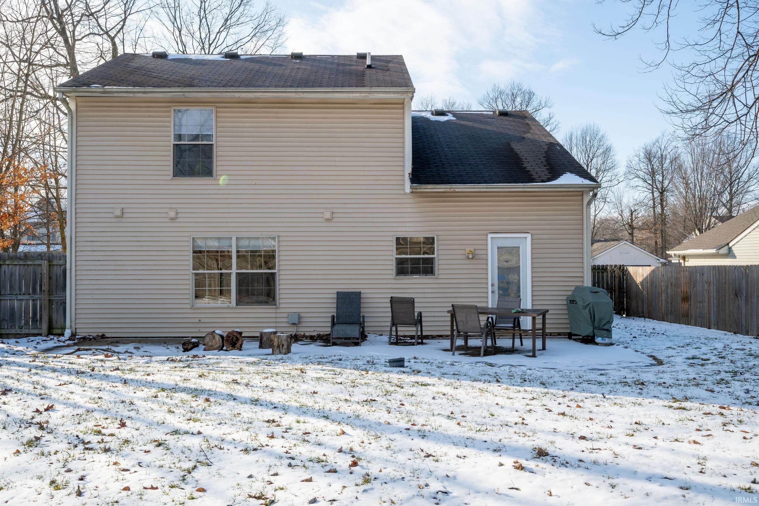 Snow covered rear of property with a fenced backyard, a patio, and roof with shingles