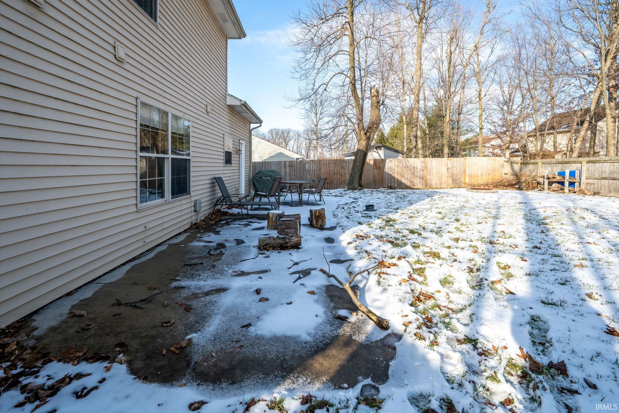 Yard layered in snow with a fenced backyard and a patio