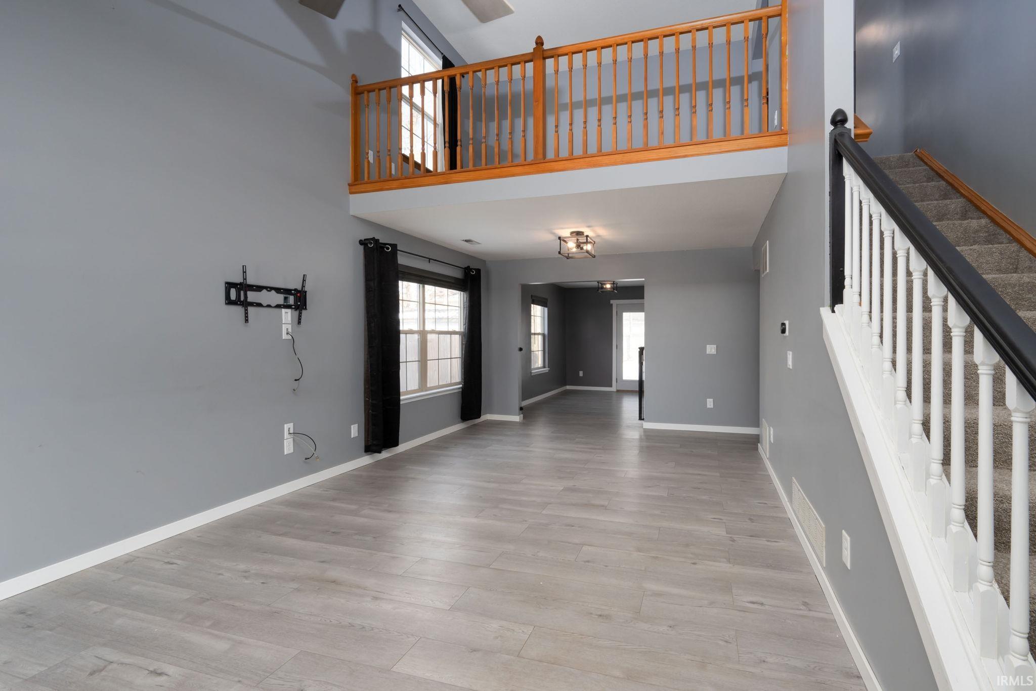 Unfurnished living room featuring a high ceiling, light wood-style flooring, and stairs