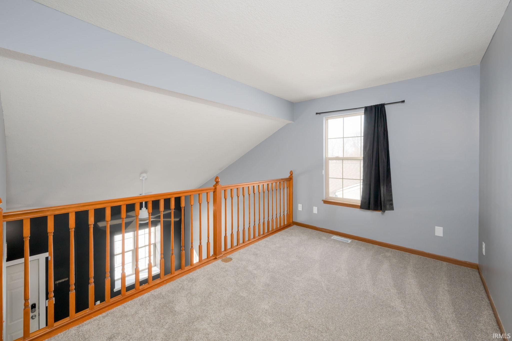 Carpeted spare room featuring baseboards and lofted ceiling