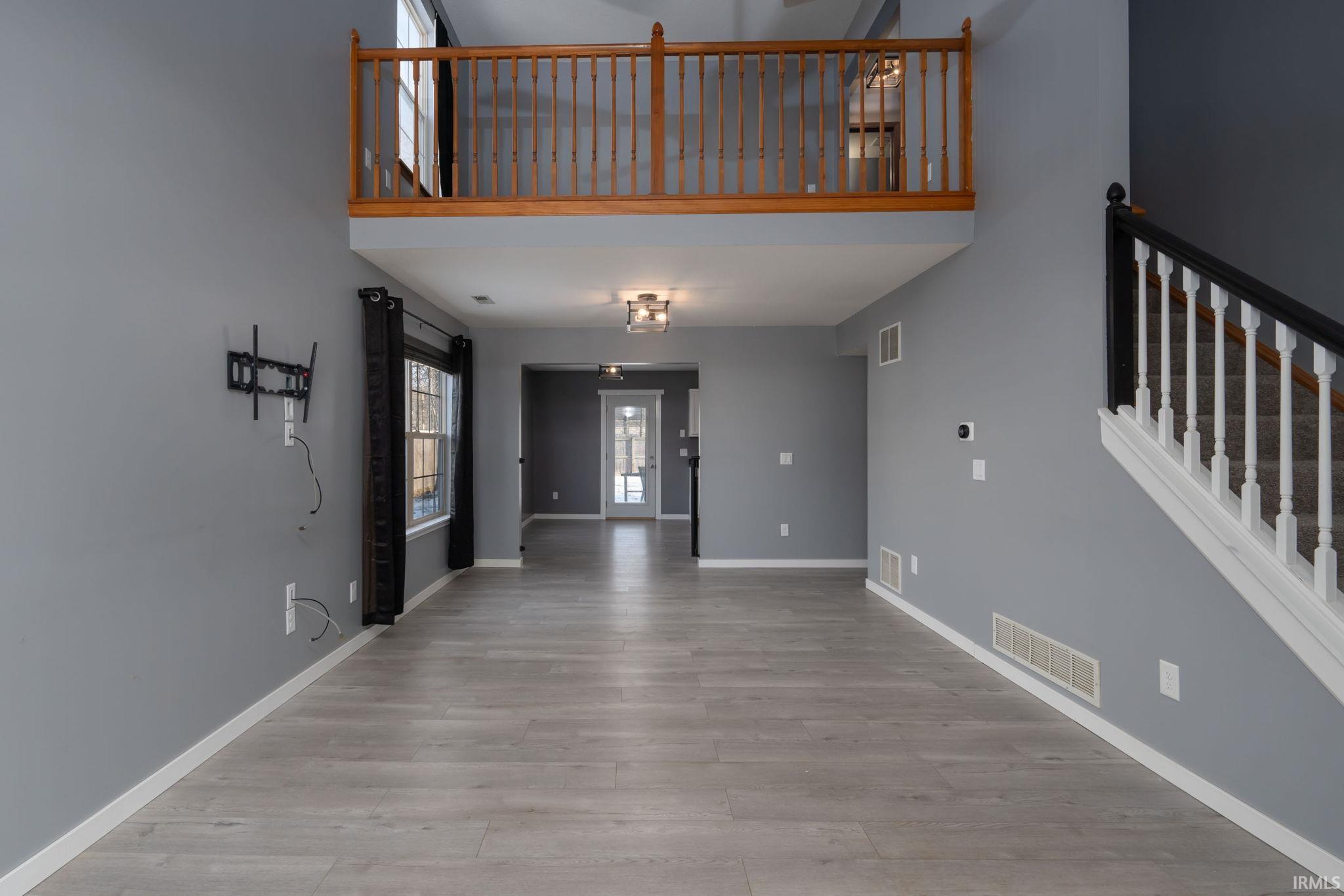 Unfurnished living room featuring stairway, a high ceiling, and light wood finished floors