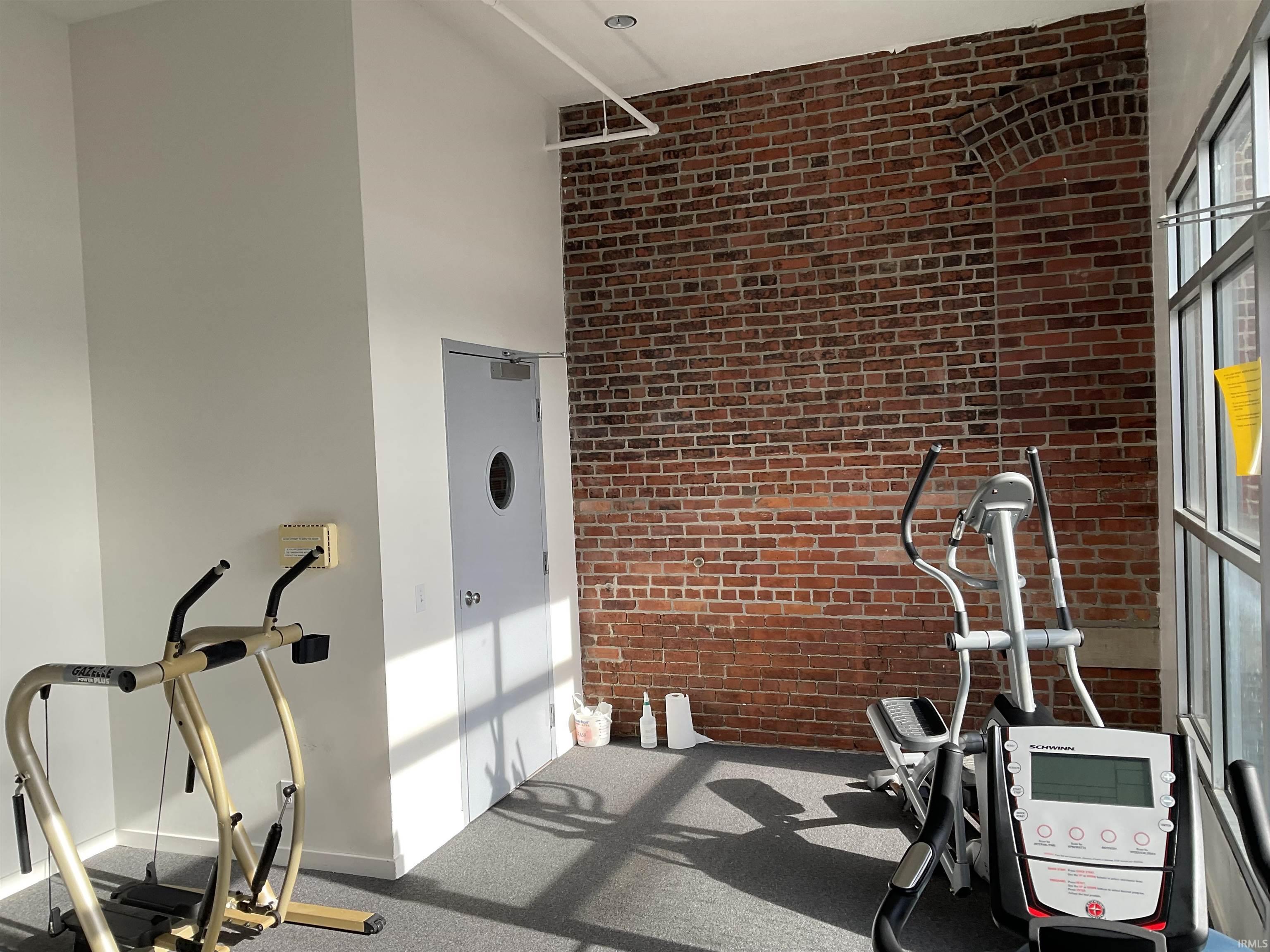 Workout room with brick wall, a towering ceiling, and carpet flooring