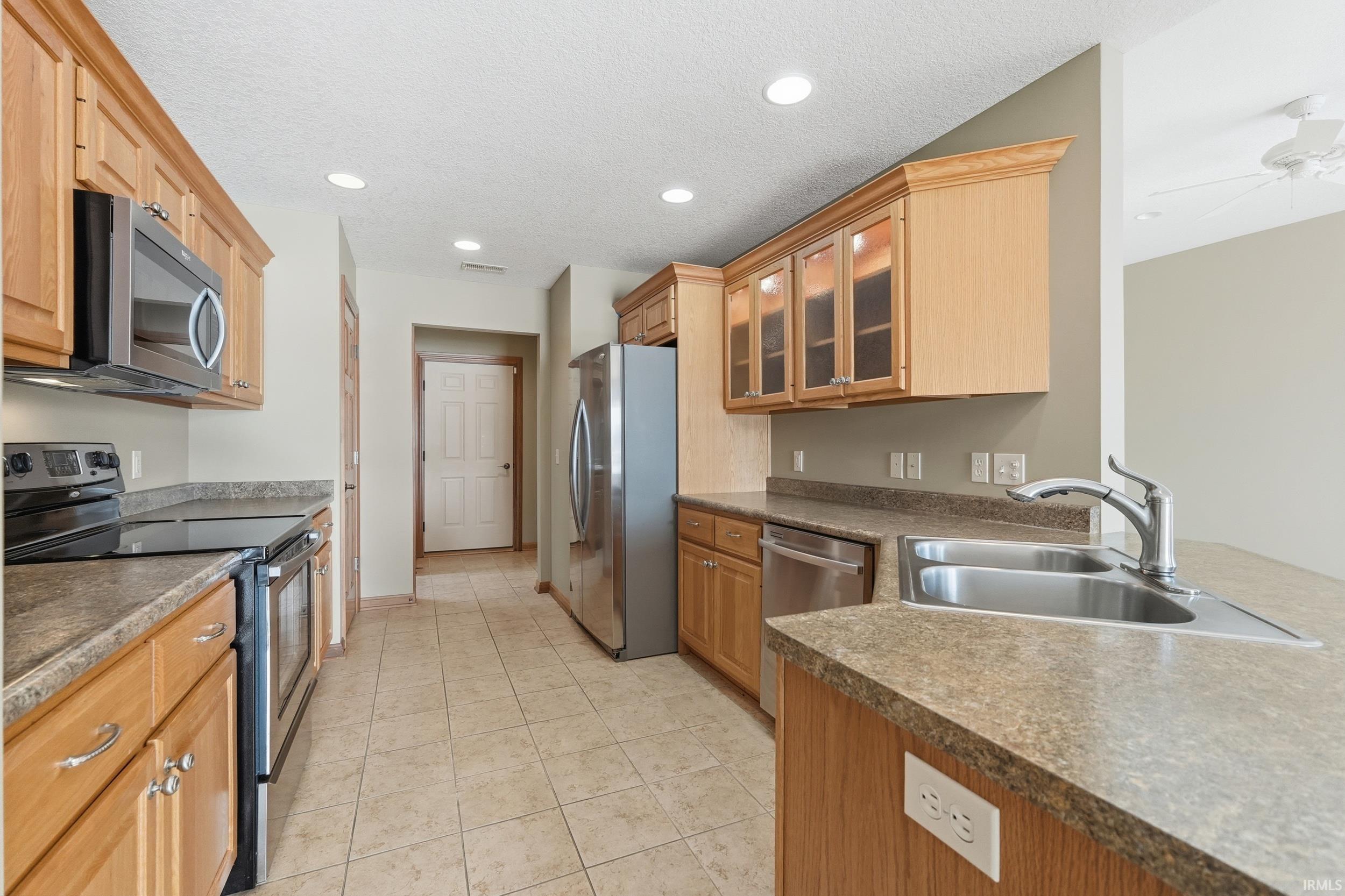 Kitchen featuring stainless steel appliances, glass insert cabinets, recessed lighting, a textured ceiling, and light tile patterned floors