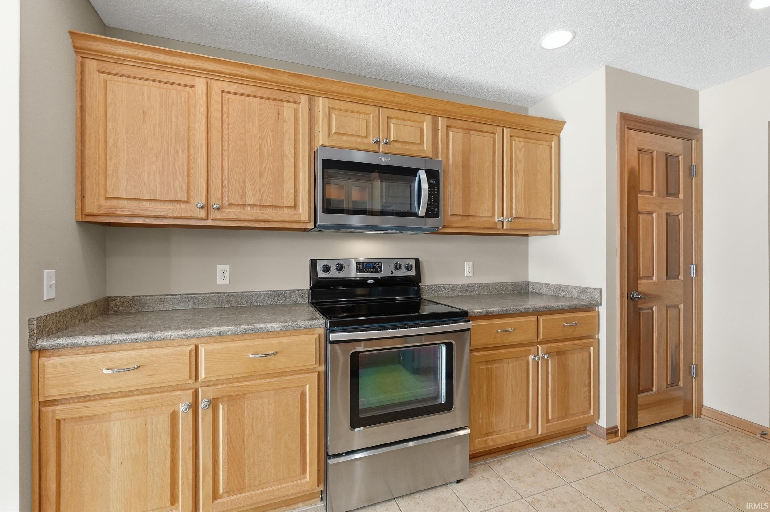 Kitchen with appliances with stainless steel finishes, a textured ceiling, light tile patterned flooring, dark countertops, and recessed lighting