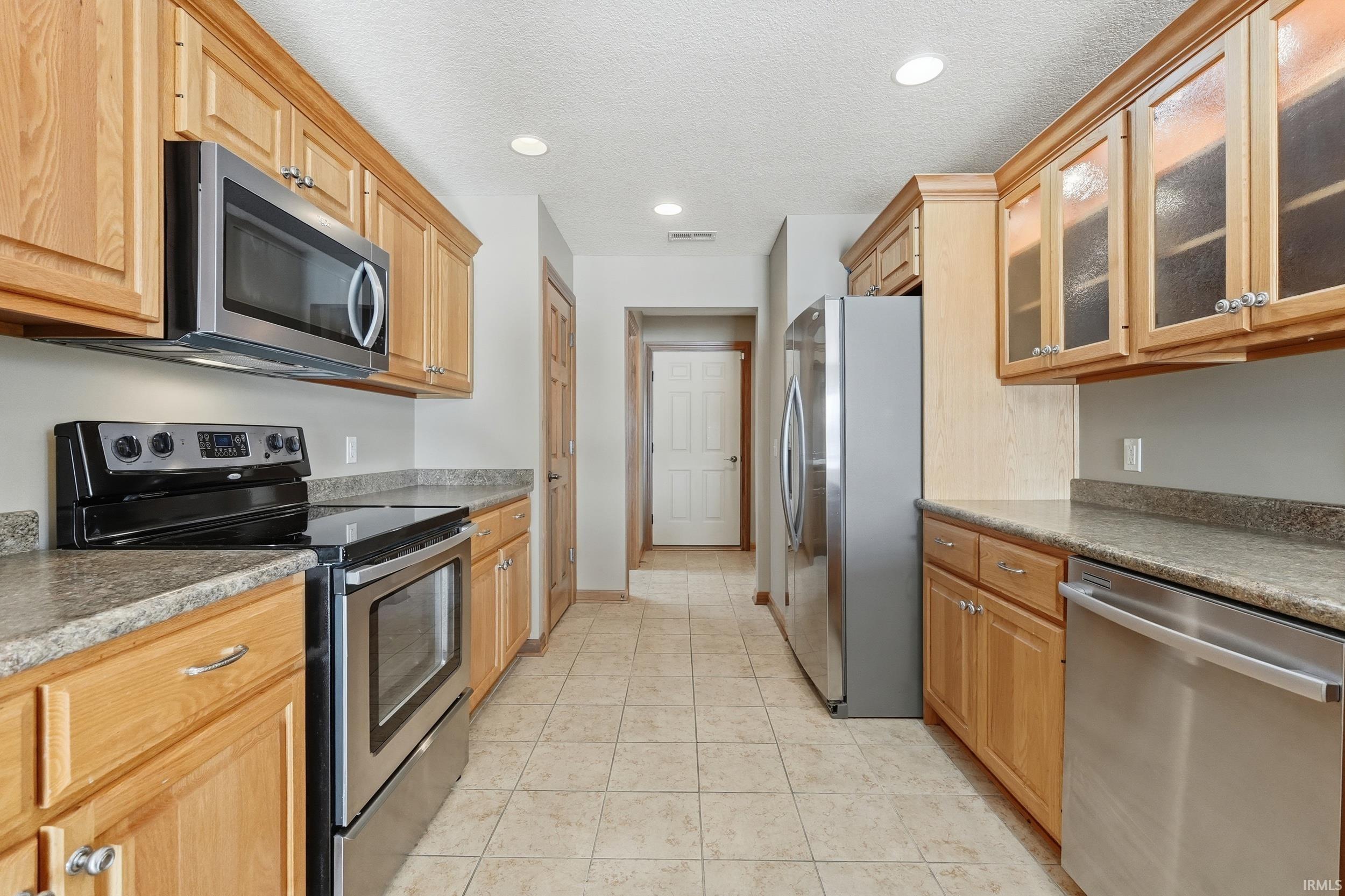 Kitchen featuring stainless steel appliances, glass insert cabinets, recessed lighting, and a textured ceiling