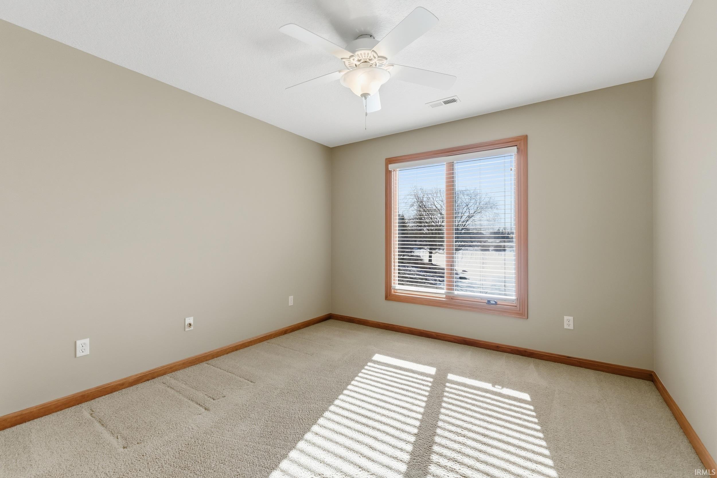 Empty room with light colored carpet and a ceiling fan