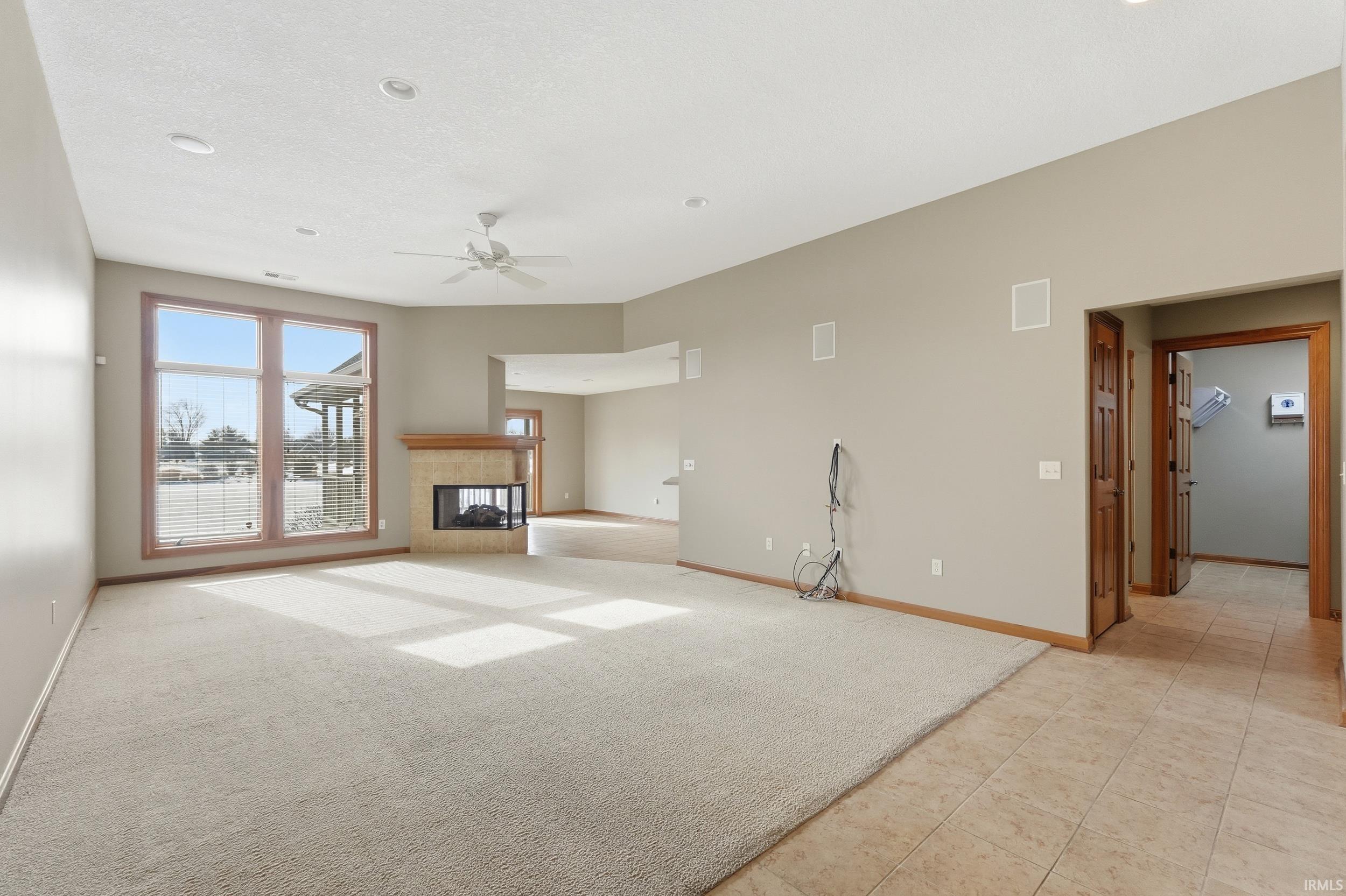 Unfurnished living room featuring a fireplace, ceiling fan, and light carpet
