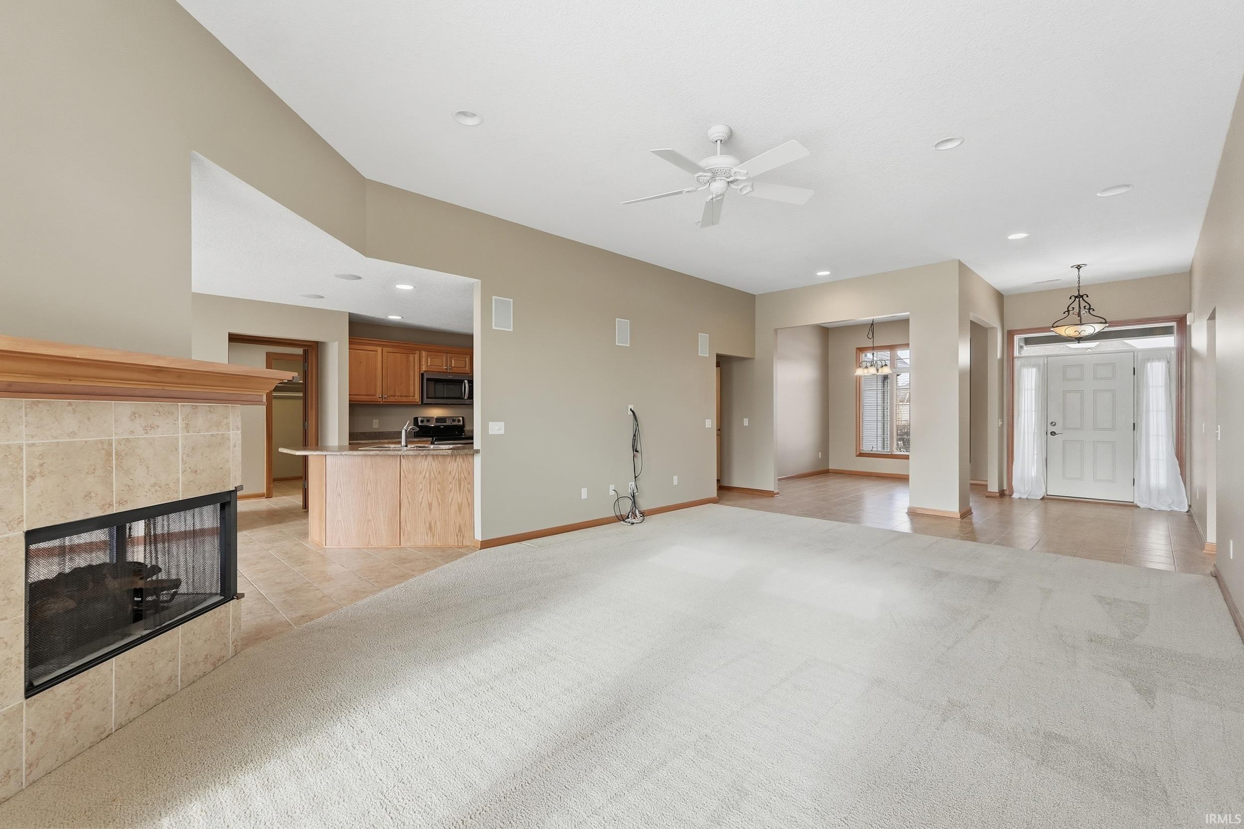 Unfurnished living room with a fireplace, a ceiling fan, recessed lighting, light carpet, and a chandelier