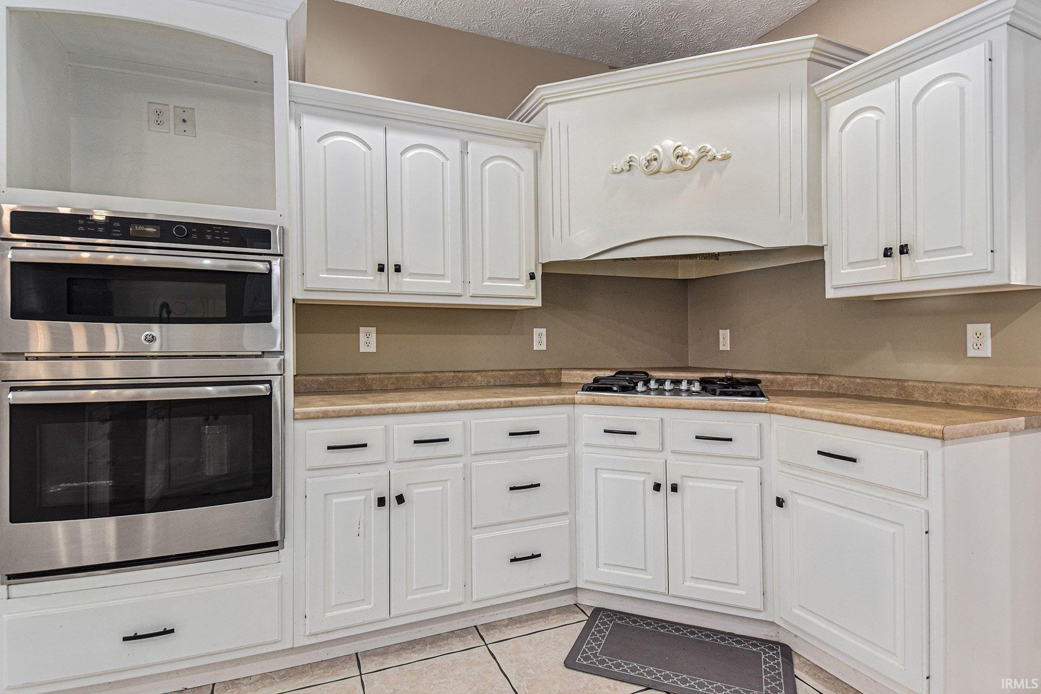 Kitchen with stainless steel appliances, light countertops, light tile patterned flooring, white cabinetry, and a textured ceiling