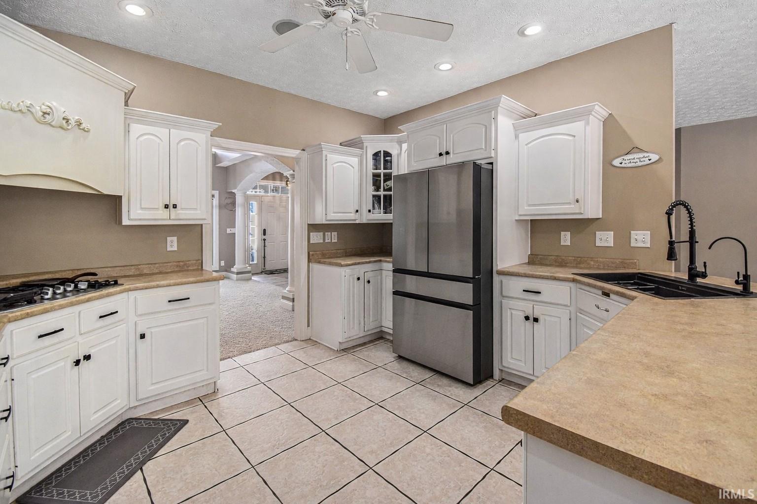 Kitchen with appliances with stainless steel finishes, arched walkways, white cabinets, a textured ceiling, and recessed lighting