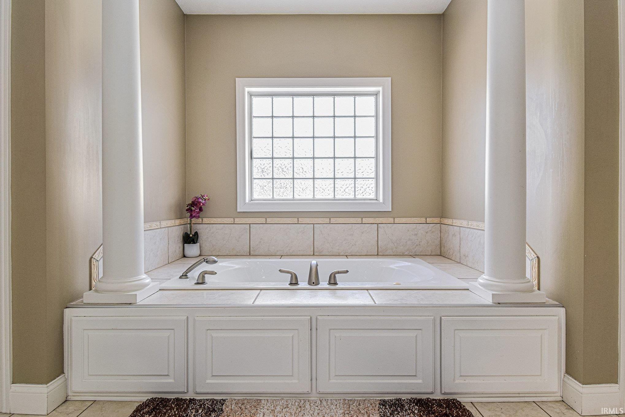 Full bathroom featuring a garden tub, tile patterned floors, and ornate columns