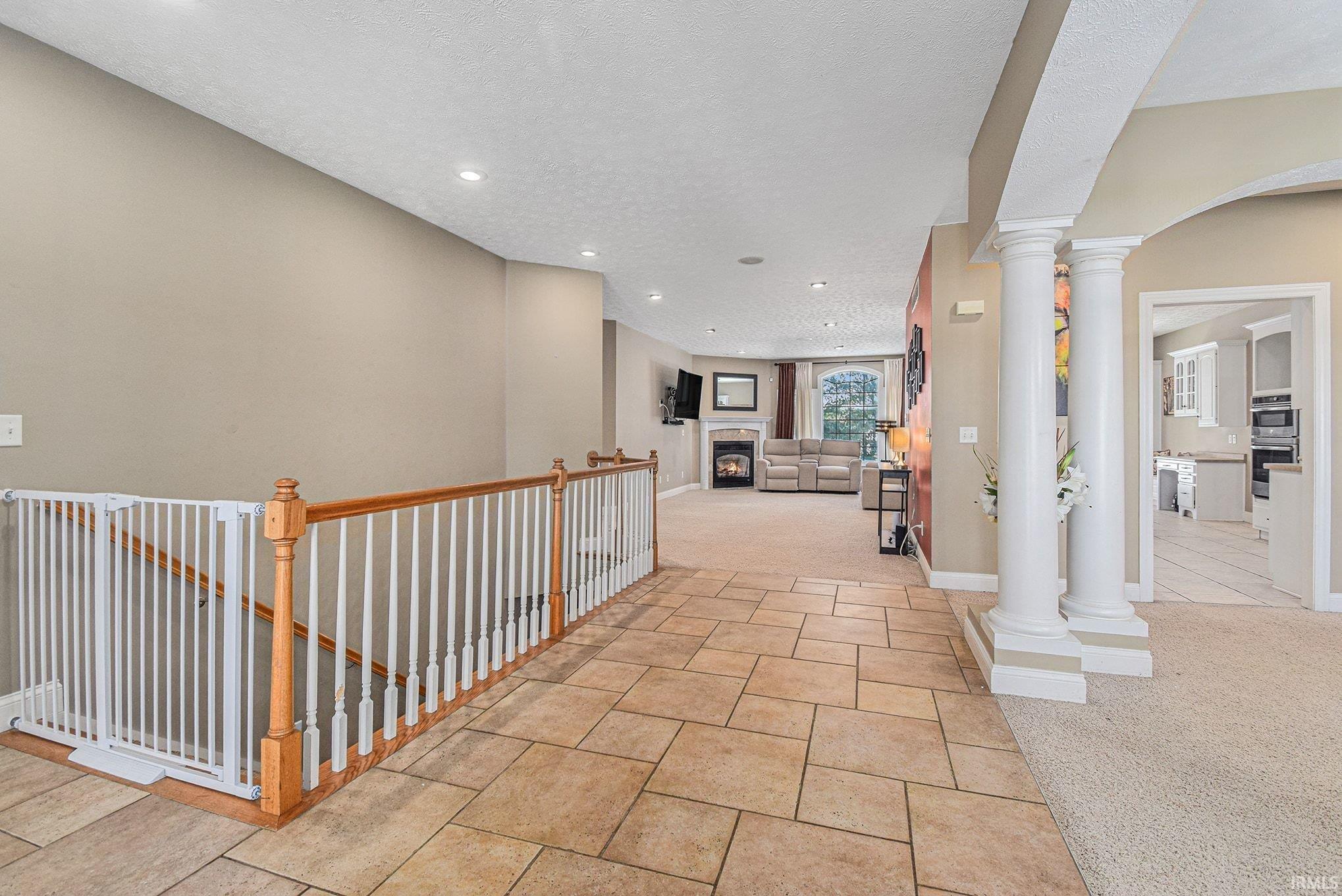 Hallway with light carpet, decorative columns, light tile patterned floors, a textured ceiling, and recessed lighting