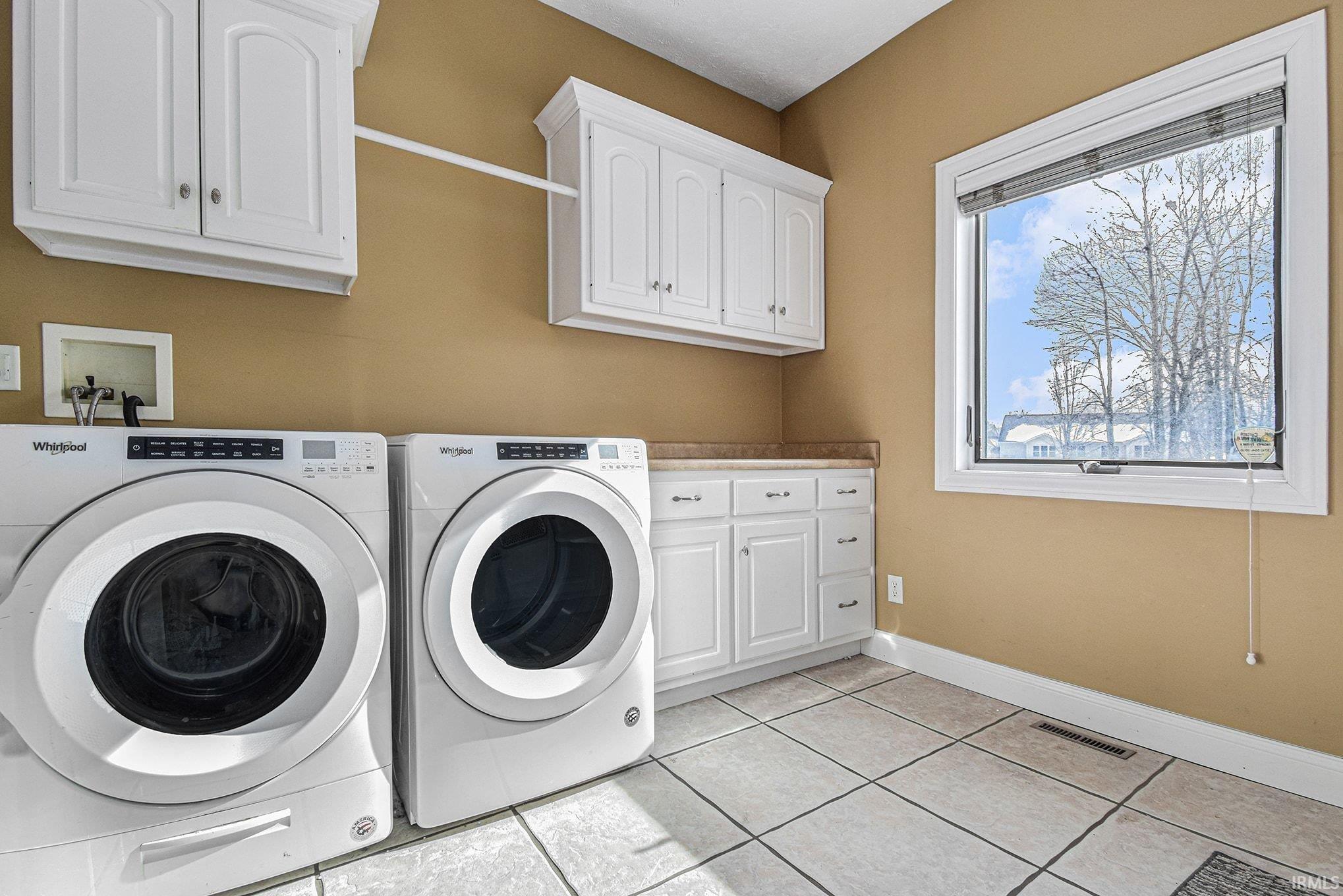 Washroom featuring light tile patterned flooring, washing machine and dryer, and cabinet space