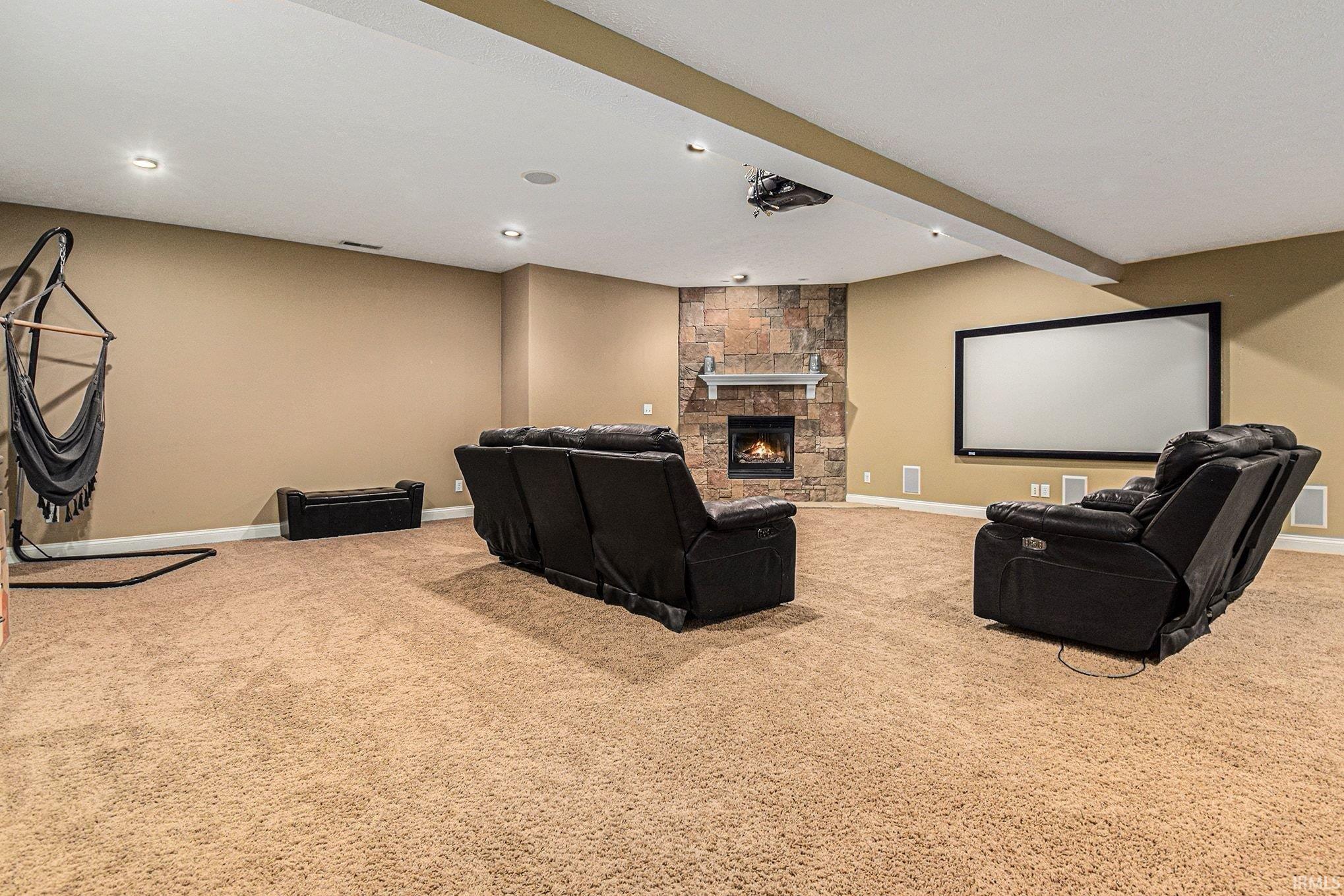 Home theater room with light colored carpet, a fireplace, and beamed ceiling